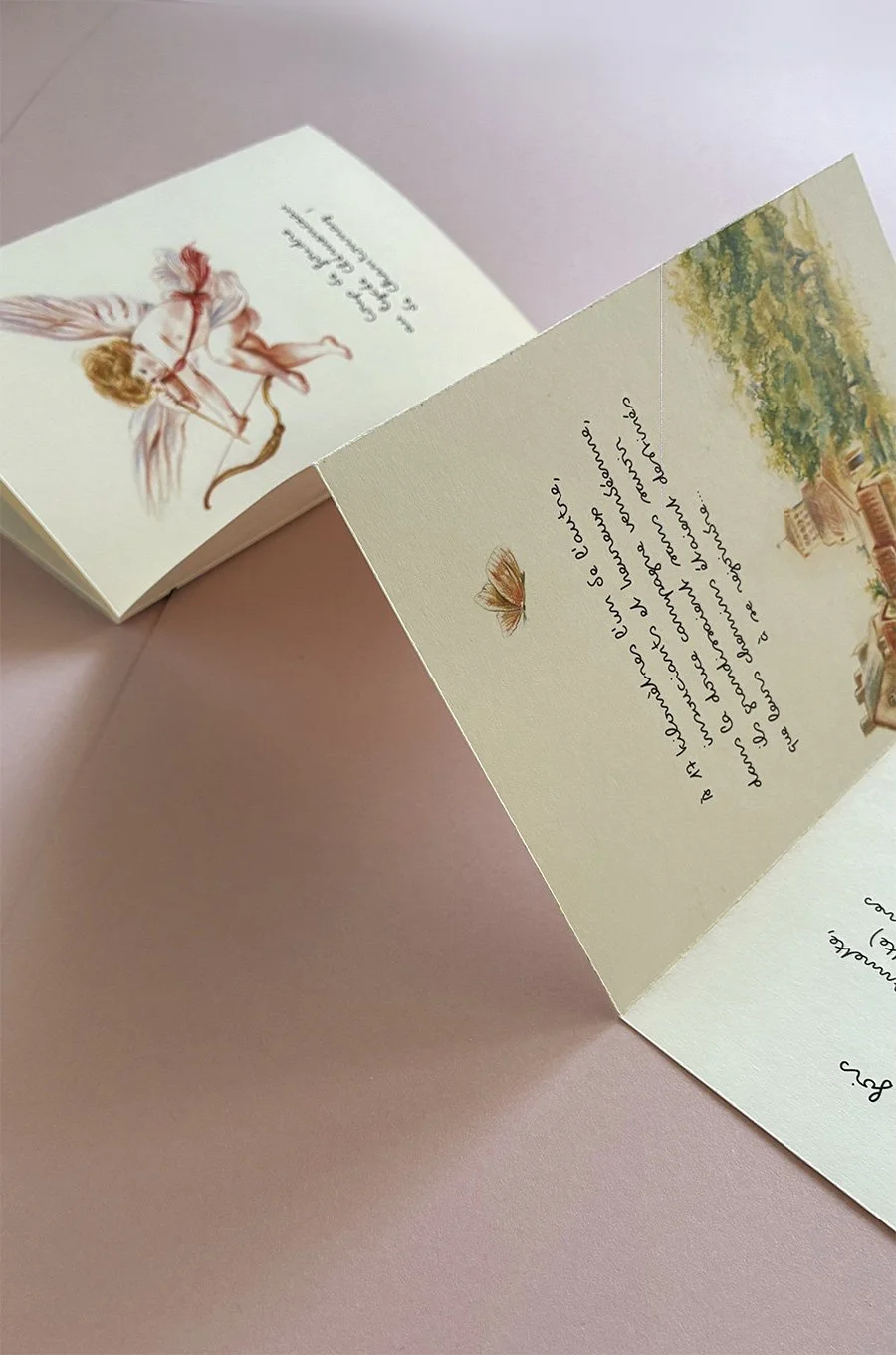 Une carte de vœux pliée avec une illustration d'un ange avec des ailes et une couronne, posée sur une surface rose, avec le texte en français écrit à l'intérieur et une petite illustration de papillon.