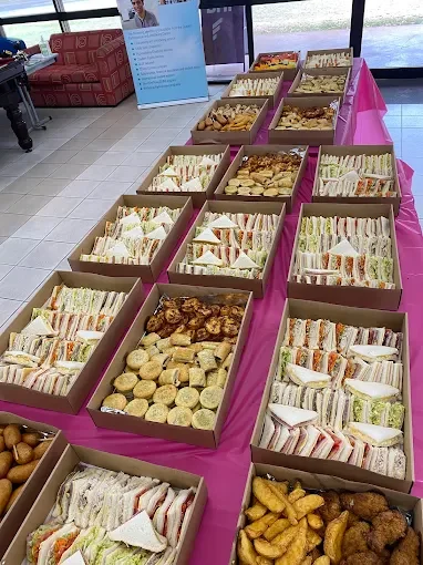 A table with multiple tables filled with sandwiches, cookies, and fried snacks at an event or gathering.
