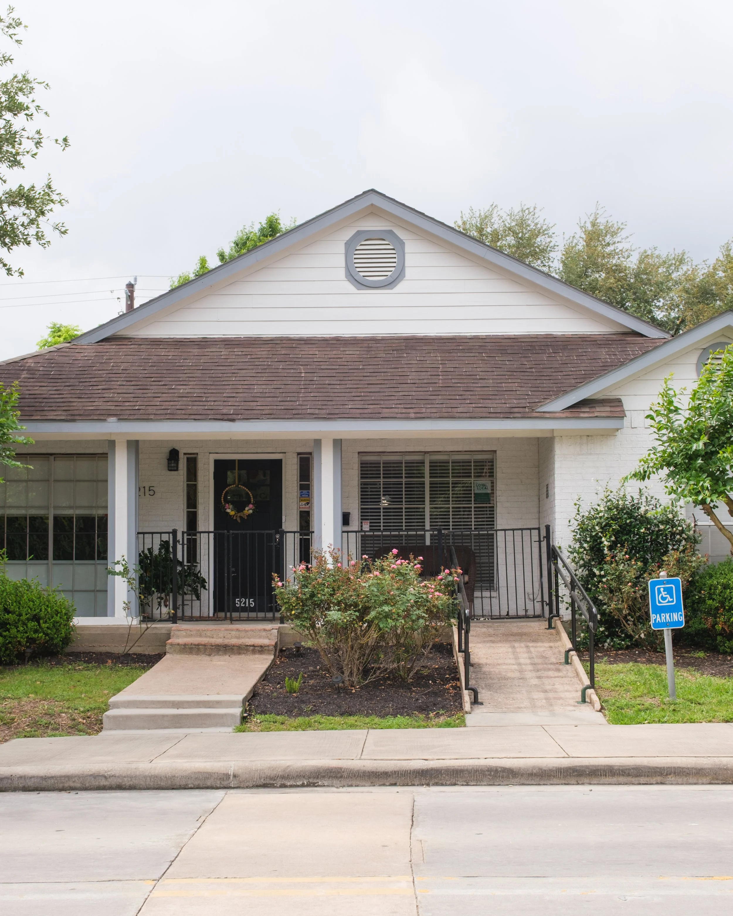 Front of a house with a small porch, a flower bed, and a handicapped parking sign on the sidewalk.