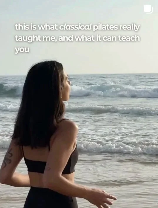 A woman with dark hair in a black sports top standing by the ocean, looking at the waves during sunset. Text overlay says, 'this is what classical Pilates really taught me, and what it can teach you.'