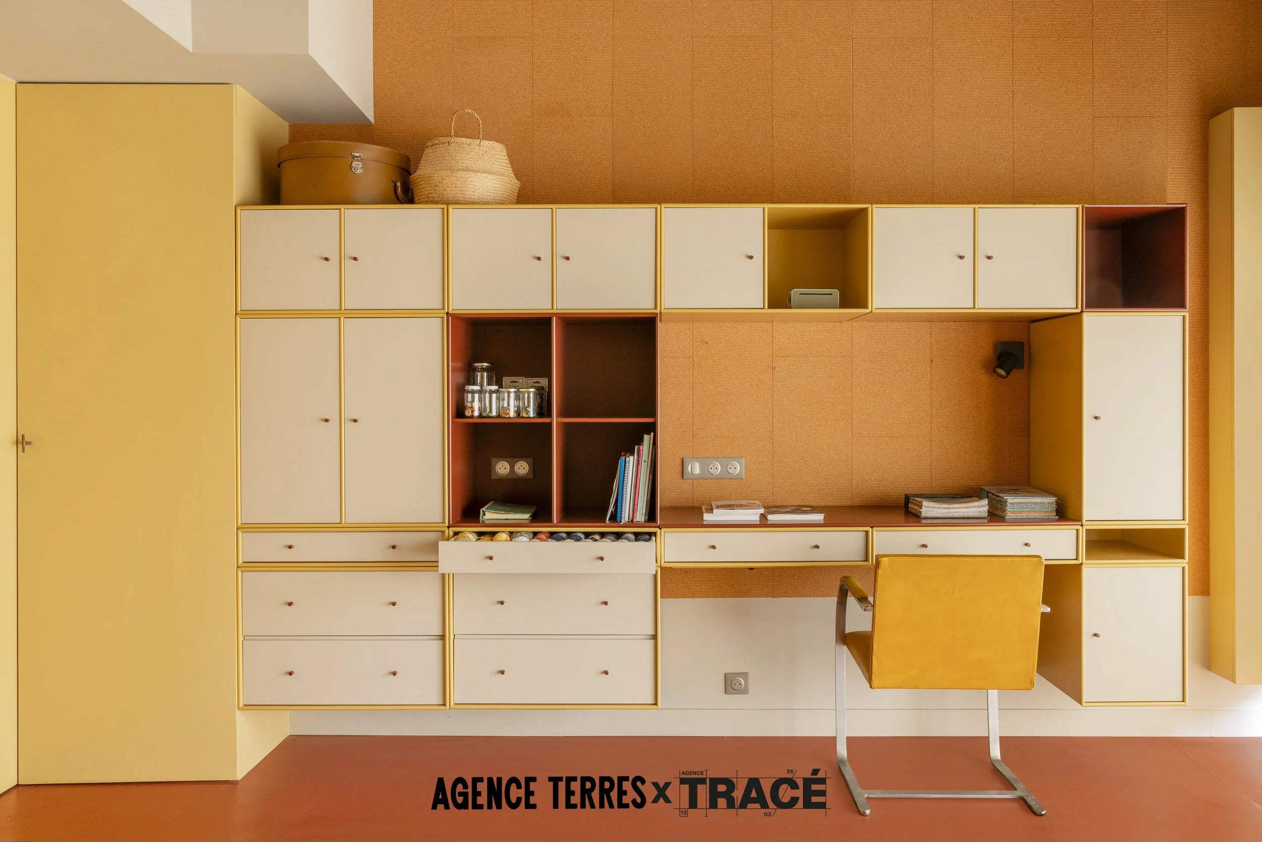Mur entièrement agencé avec des meubles sur mesure colorés pour création d'un atelier de création multiactivités, avec pleins de zones de rangements spécifiques et adaptées. Le tout dans des coloris jaune, beige et orange.