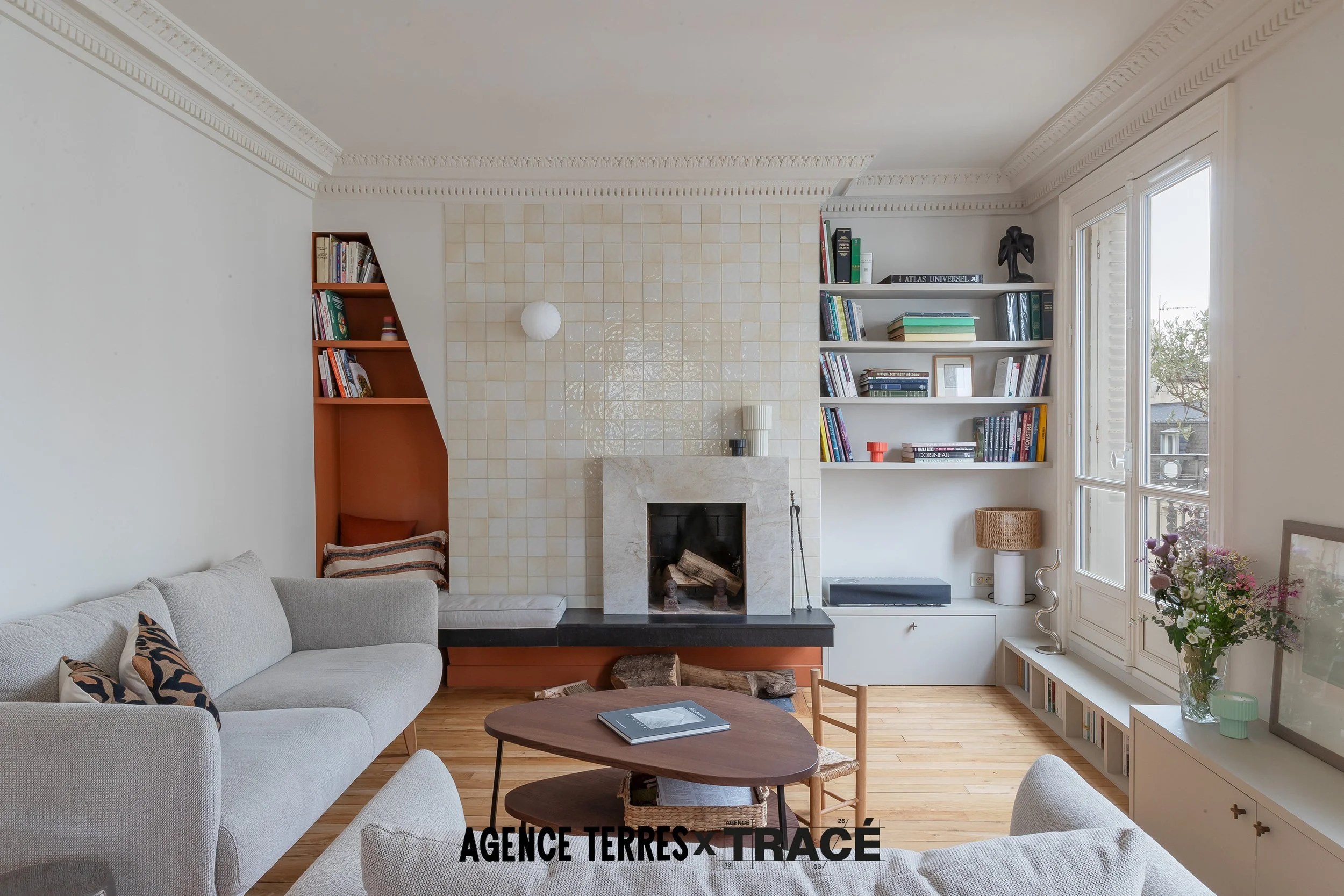 Salon rénové avec une nouvelle cheminée sur mesure en pierre naturelle, un coin lecture dans une niche colorée à gauche et une bibliothèque sur mesure à droite. Le tout dans un salon clair, chaleureux doux.