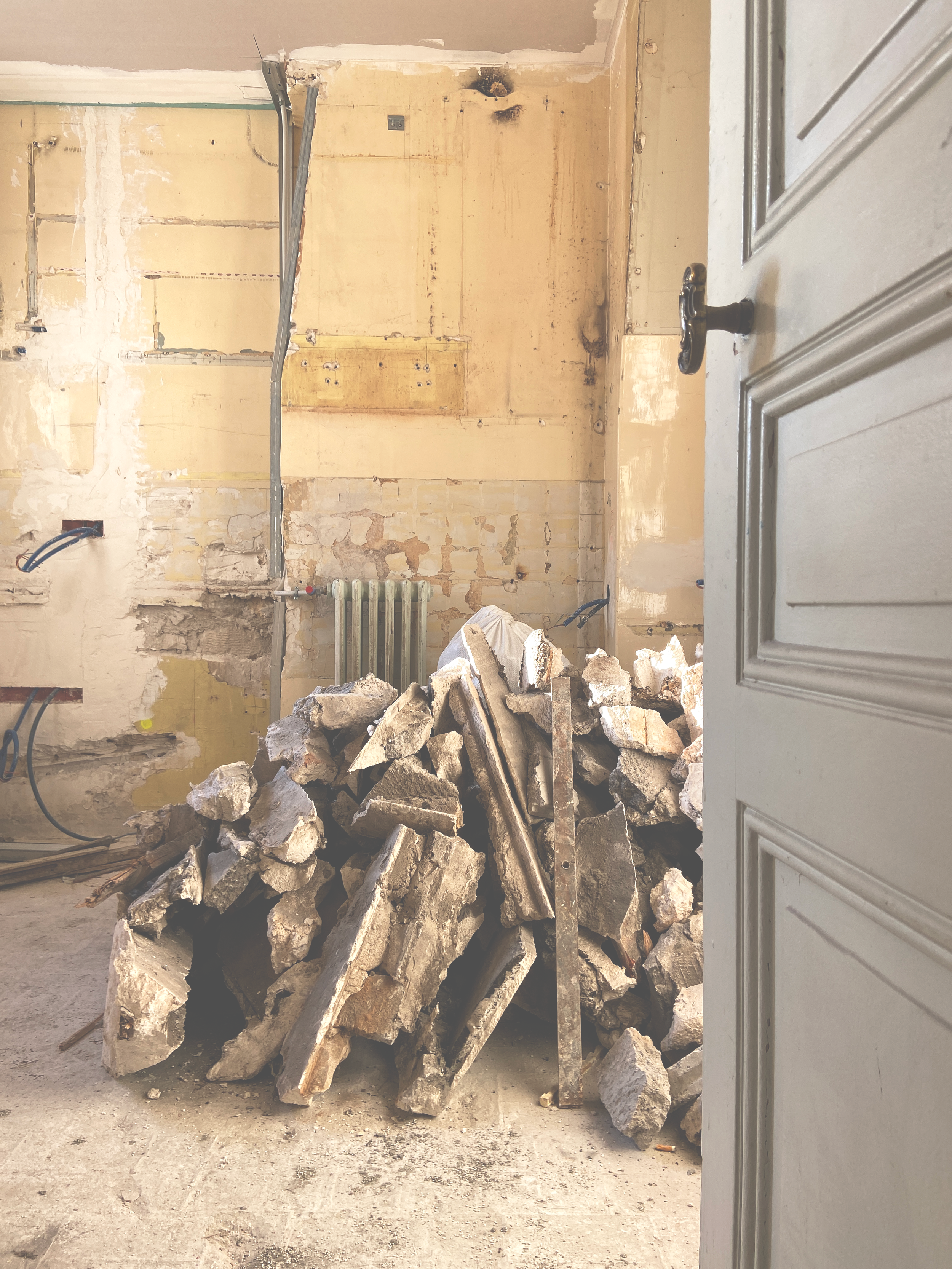 Une pièce en rénovation avec un mur cassé et des gravats au sol. Symbolise une phase de chantier dans un appartement en rénovation.