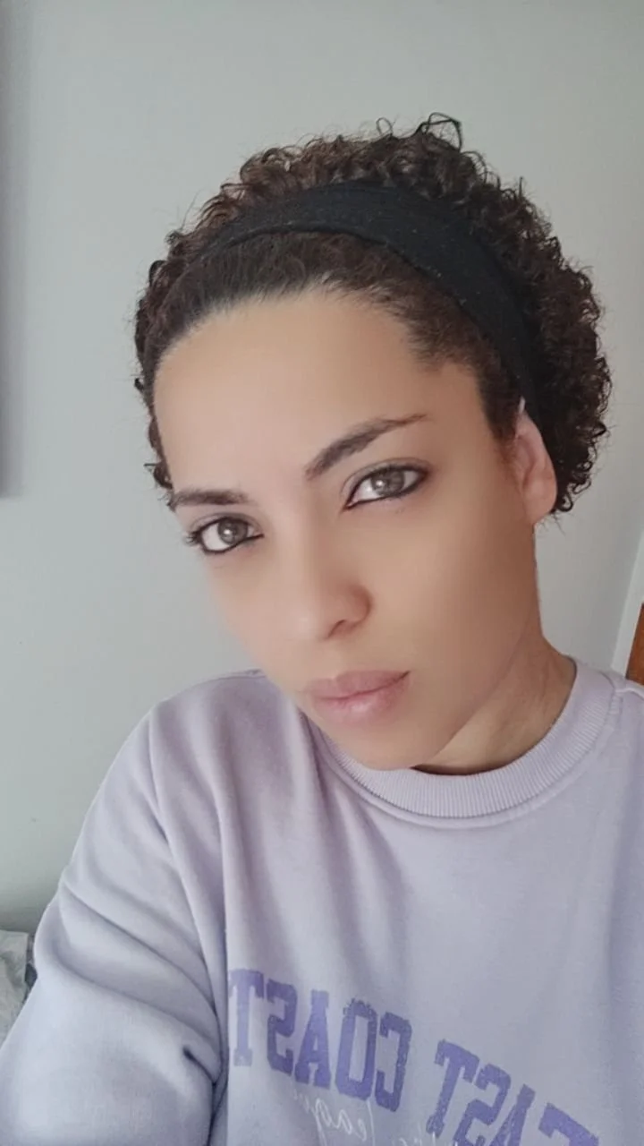 Retrato de una mujer con cabello rizado usando una diadema negra, con piel clara y ojos de color claro