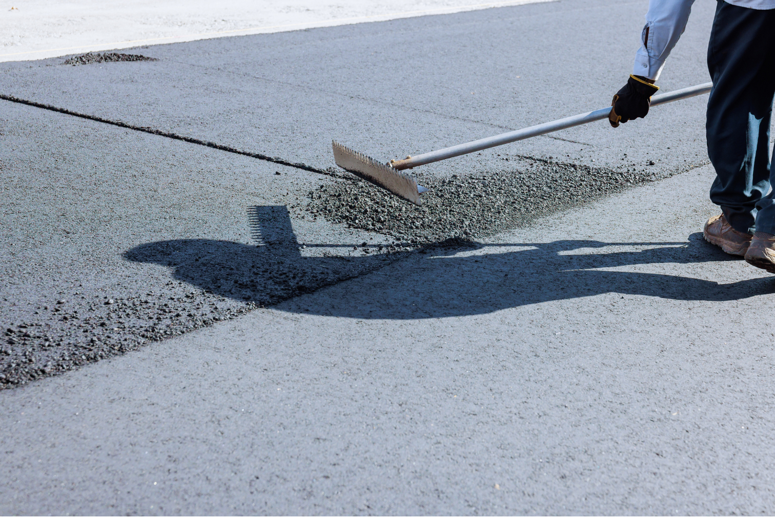 Travailleur posant du béton sur une route avec une pelle guide lors d’un chantier de construction.