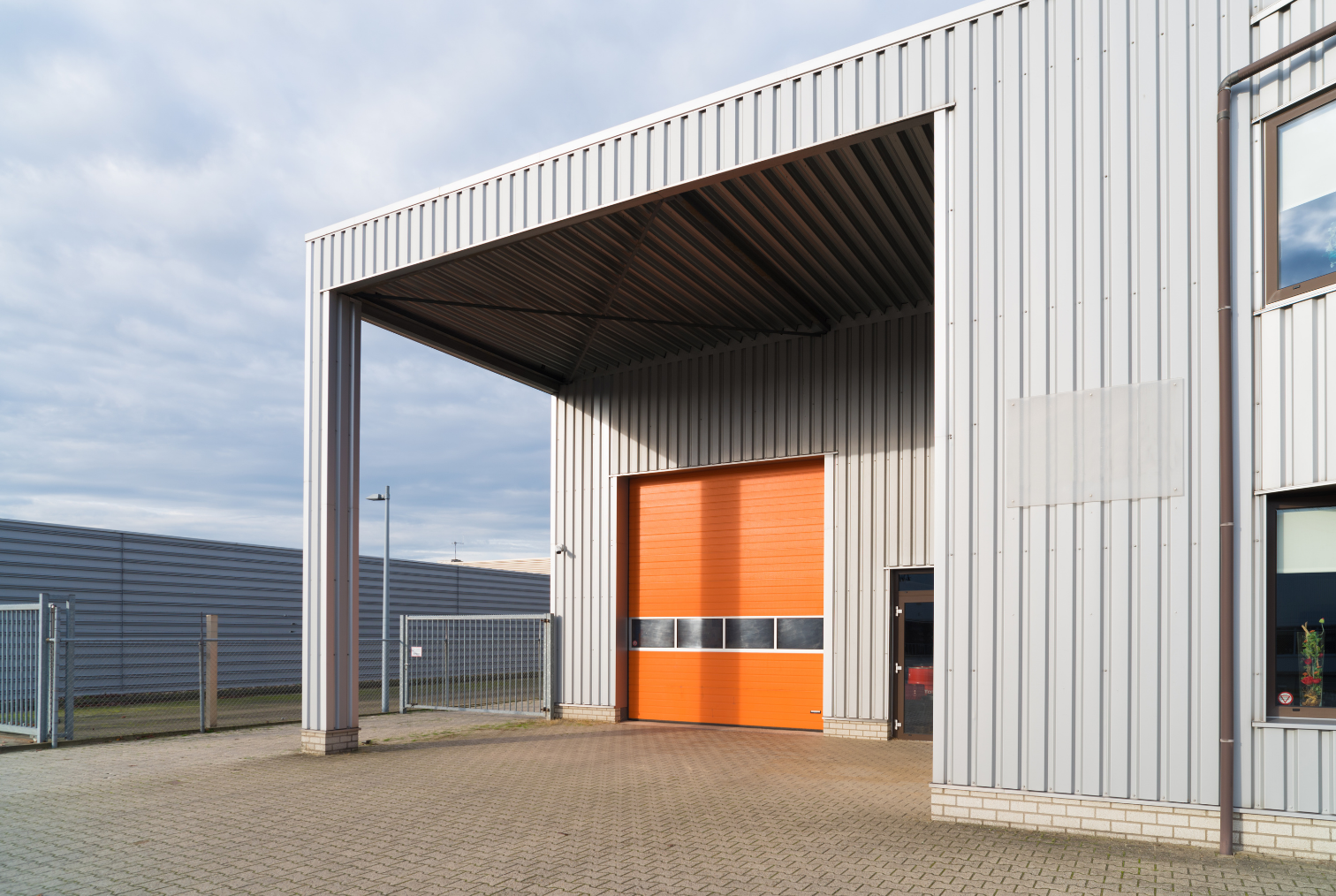 Bâtiment industriel avec un grand portail orange et une zone couverte devant.