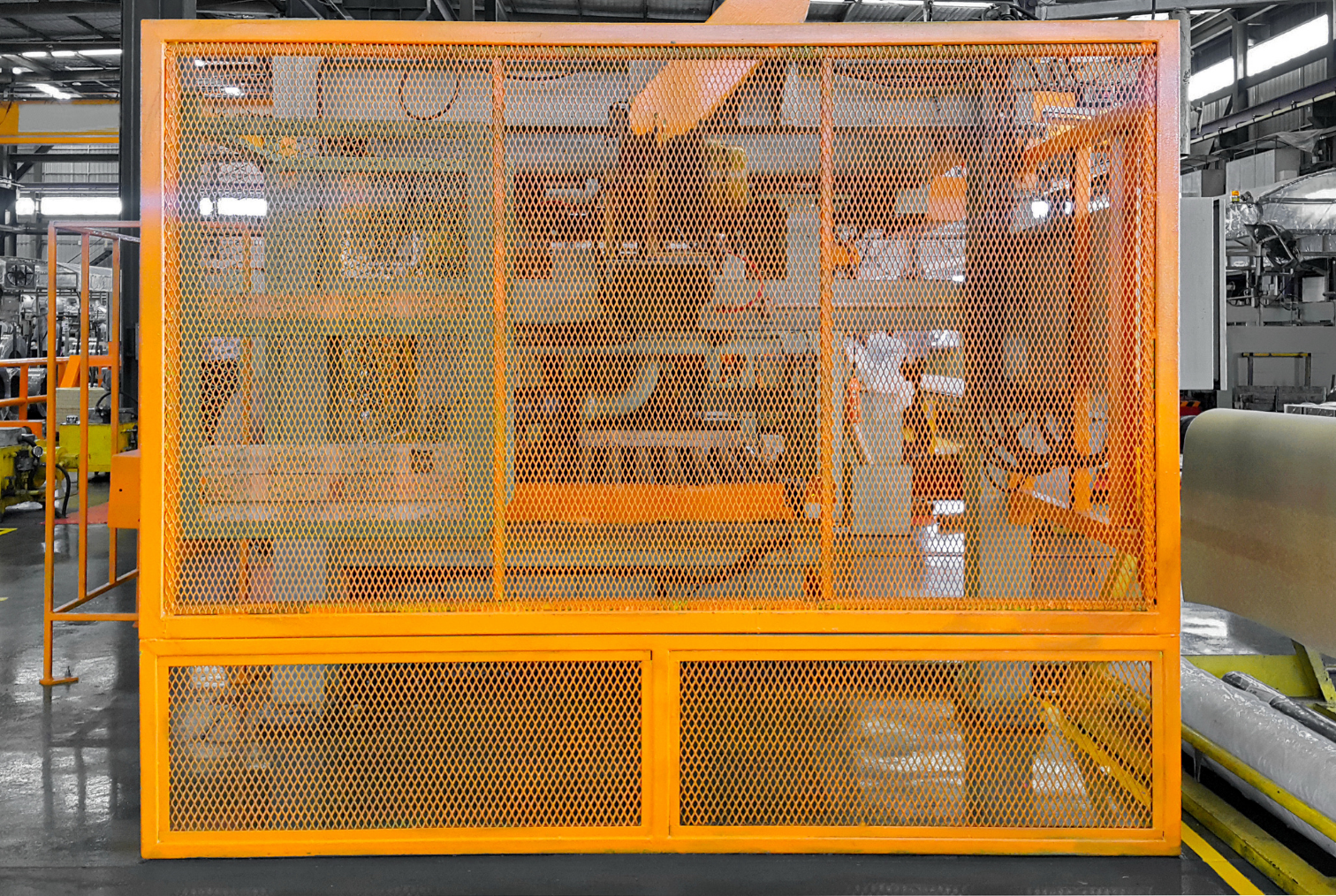 Une cage de sécurité orange dans une usine, contenant des machines industrielles. 