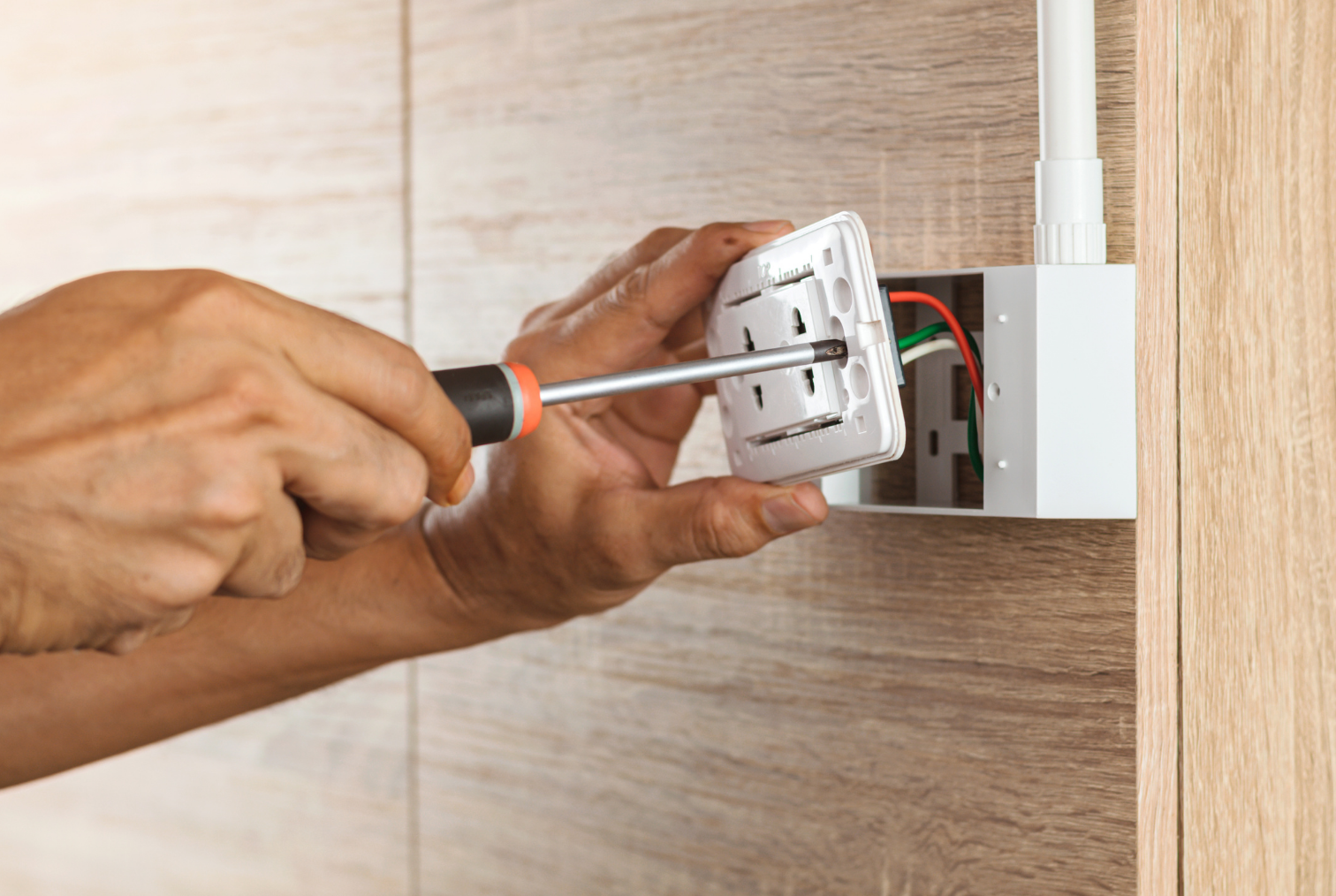 Une personne effectue des travaux d'électricité en utilisant un tournevis pour réparer une prise électrique dans un mur.