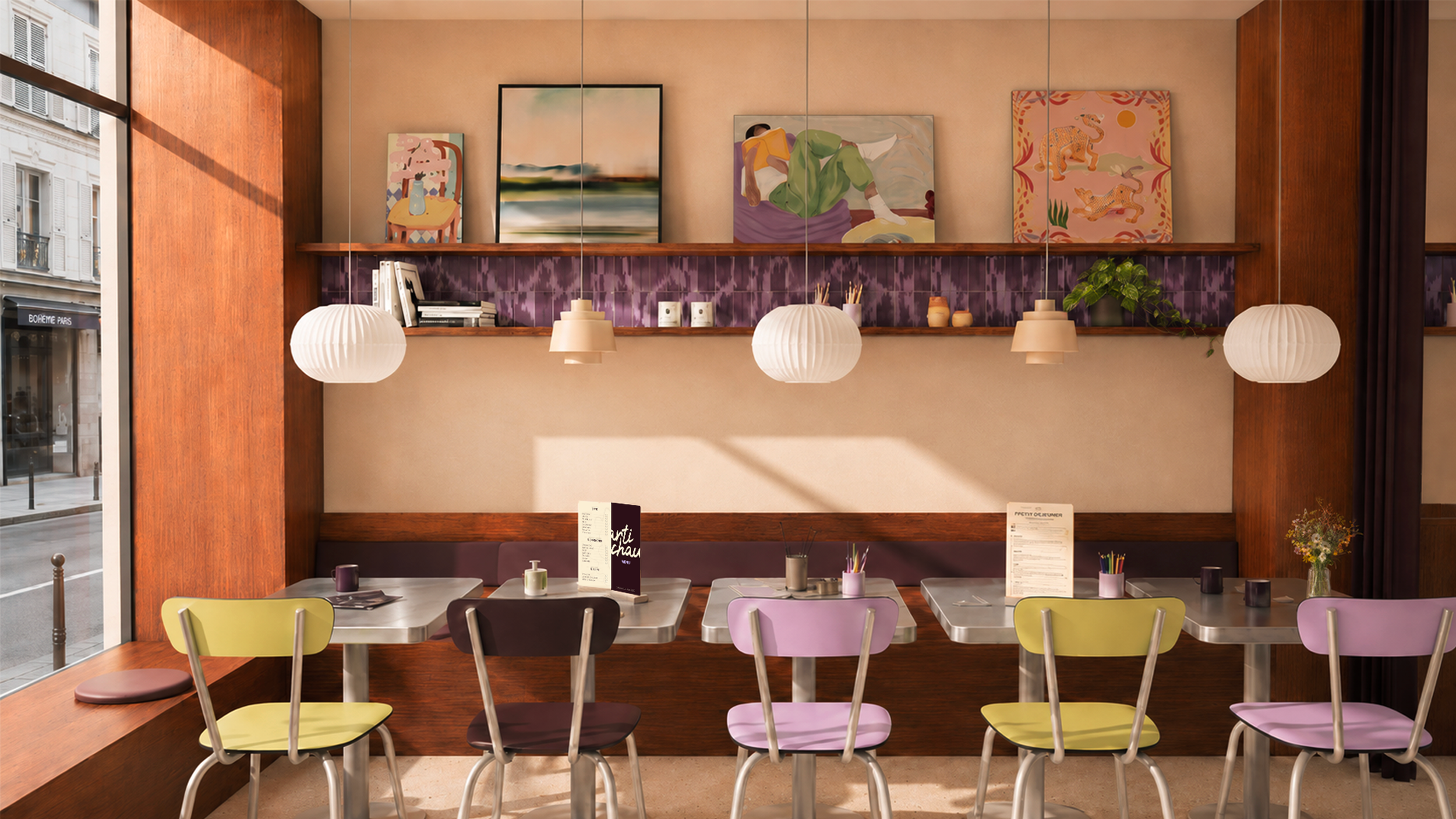 Intérieur d'un café artistique avec un mur décoré de plusieurs œuvres d'art accrochées, des lampes suspendues blanches, et des tables en inox avec des chaises colorées, près d'une façade vitrée laissant entrer la lumière naturelle.