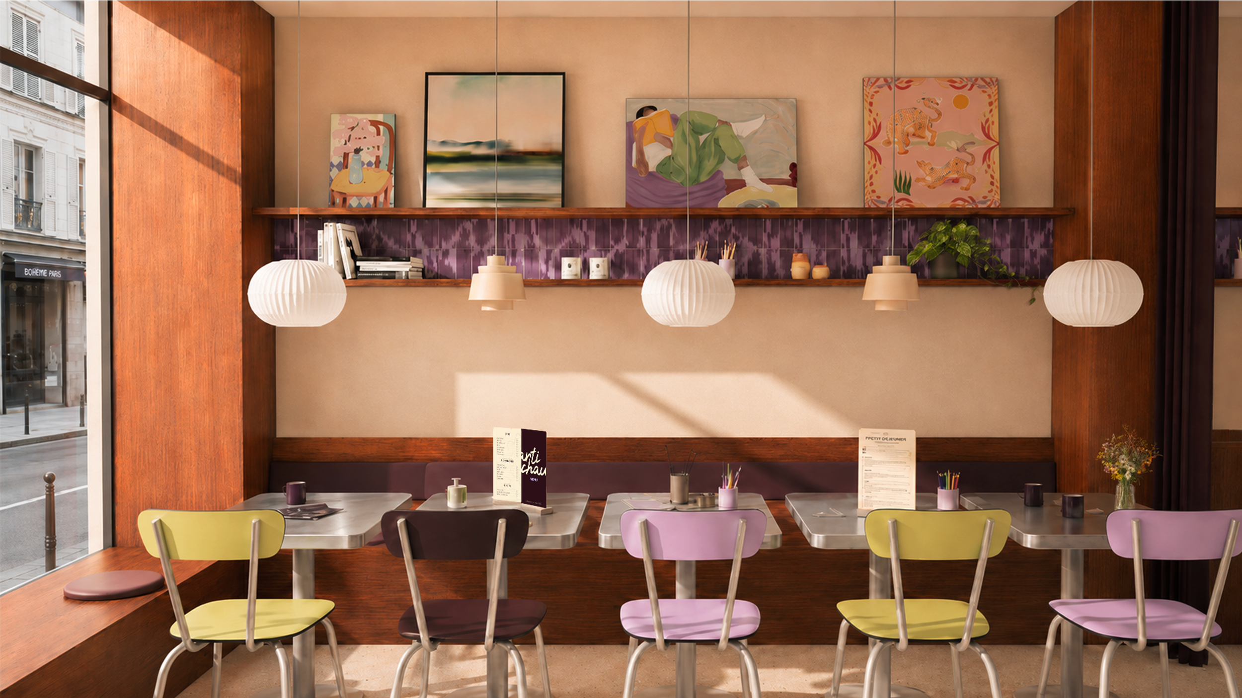 Intérieur d'un café artistique avec un mur décoré de plusieurs œuvres d'art accrochées, des lampes suspendues blanches, et des tables en inox avec des chaises colorées, près d'une façade vitrée laissant entrer la lumière naturelle.