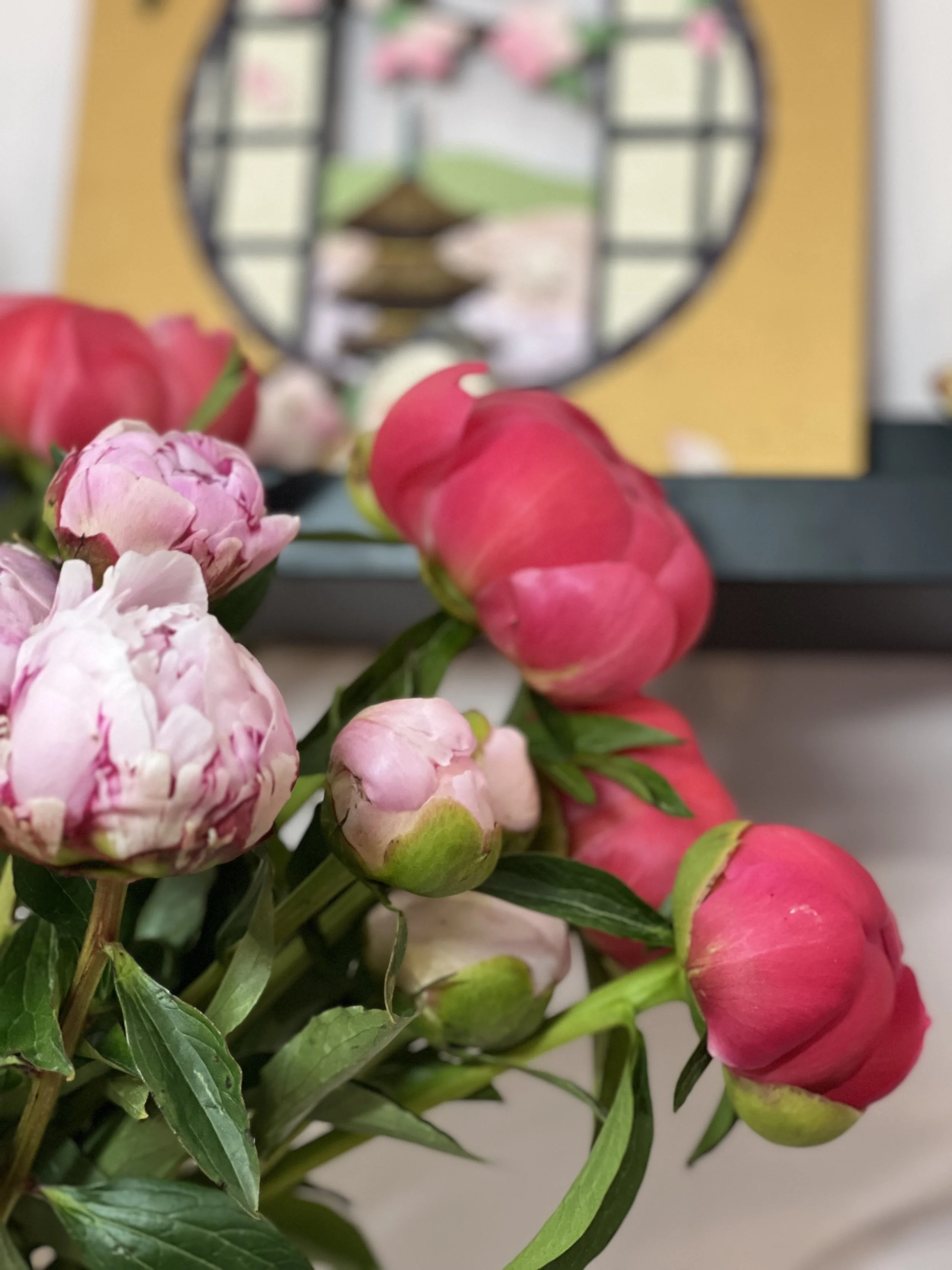 Un bouquet de fleurs avec des pivoines roses et blanches devant un miroir rond
