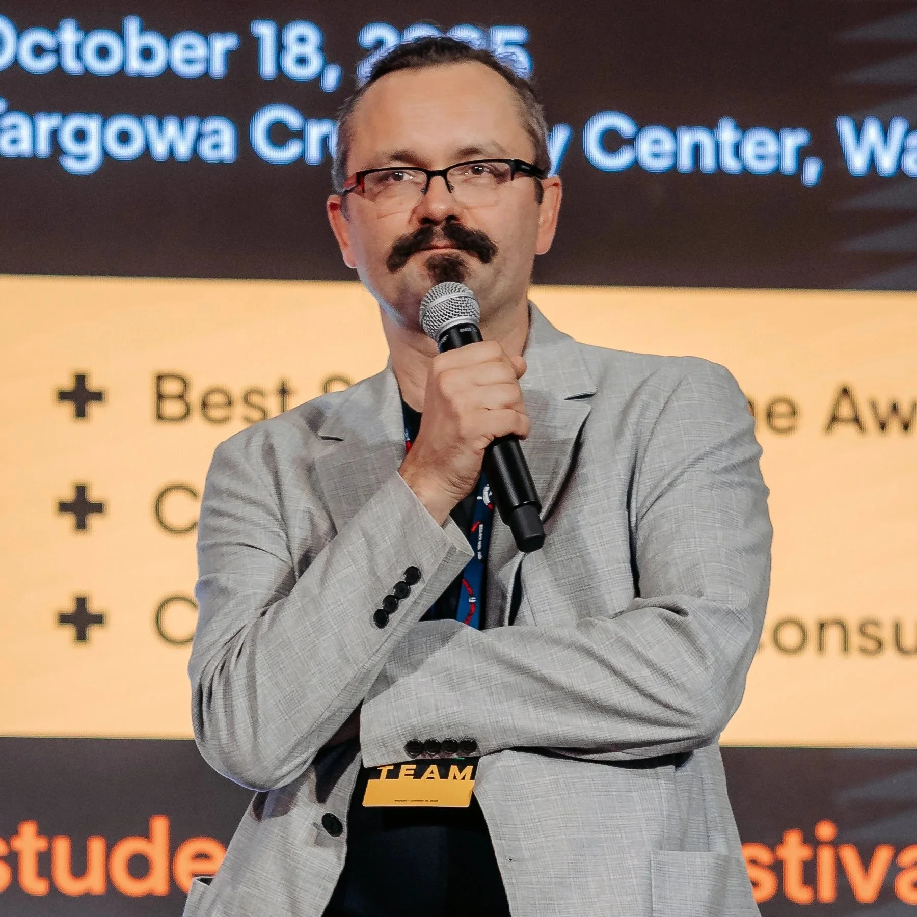 A man with glasses, a mustache, and a goatee, holding a microphone, standing in front of a background with text about an event on October 18-22, 2023, at the Georgia World Congress Center in Atlanta.