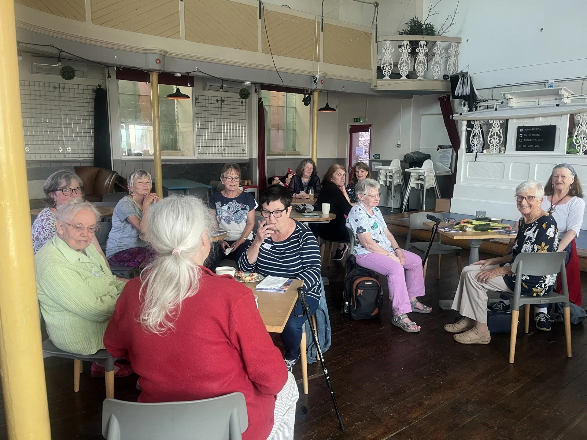 A group of elderly women sitting in our cozy café space, chatting and some drinking coffee.