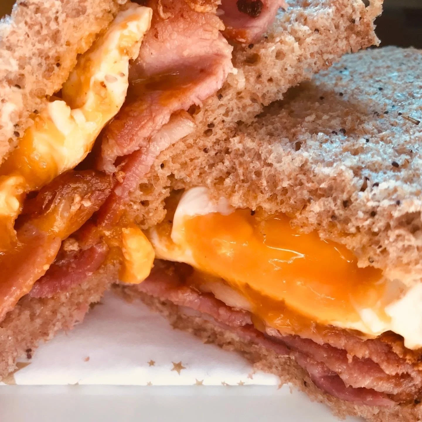 A mouth-watering close up of a breakfast sandwich with fried egg and bacon on nice brown bread.