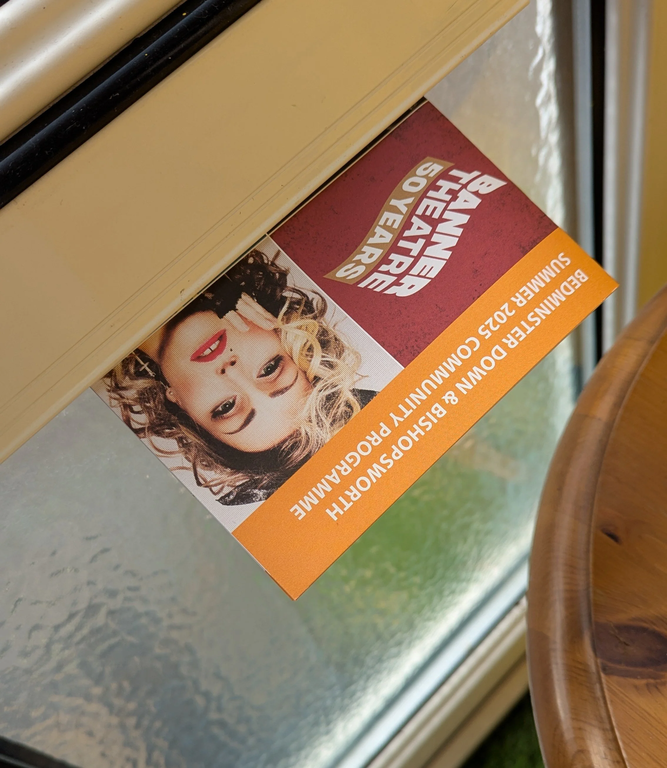Our programme with a picture of Madonna advertising the tribute act is half way posted through someone's door, with the glass of the door and the wooden side table visible in the background.