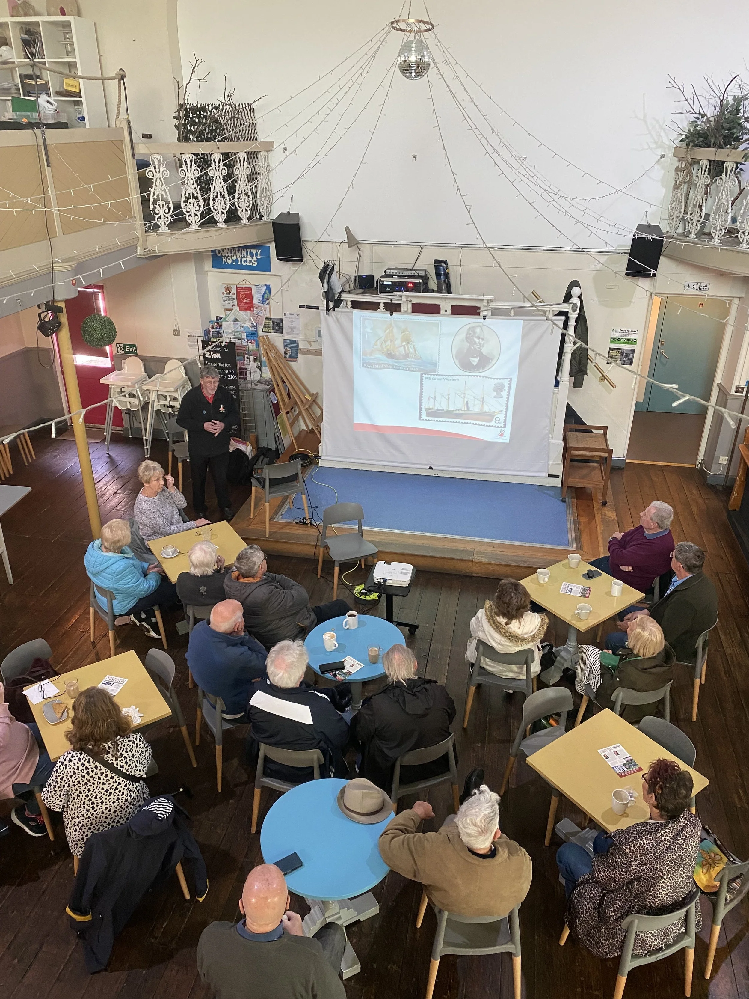 Our local history group is having a presentation by someone, with images on the screen at the front and lots of people sitting around tables enjoying coffee and learning!