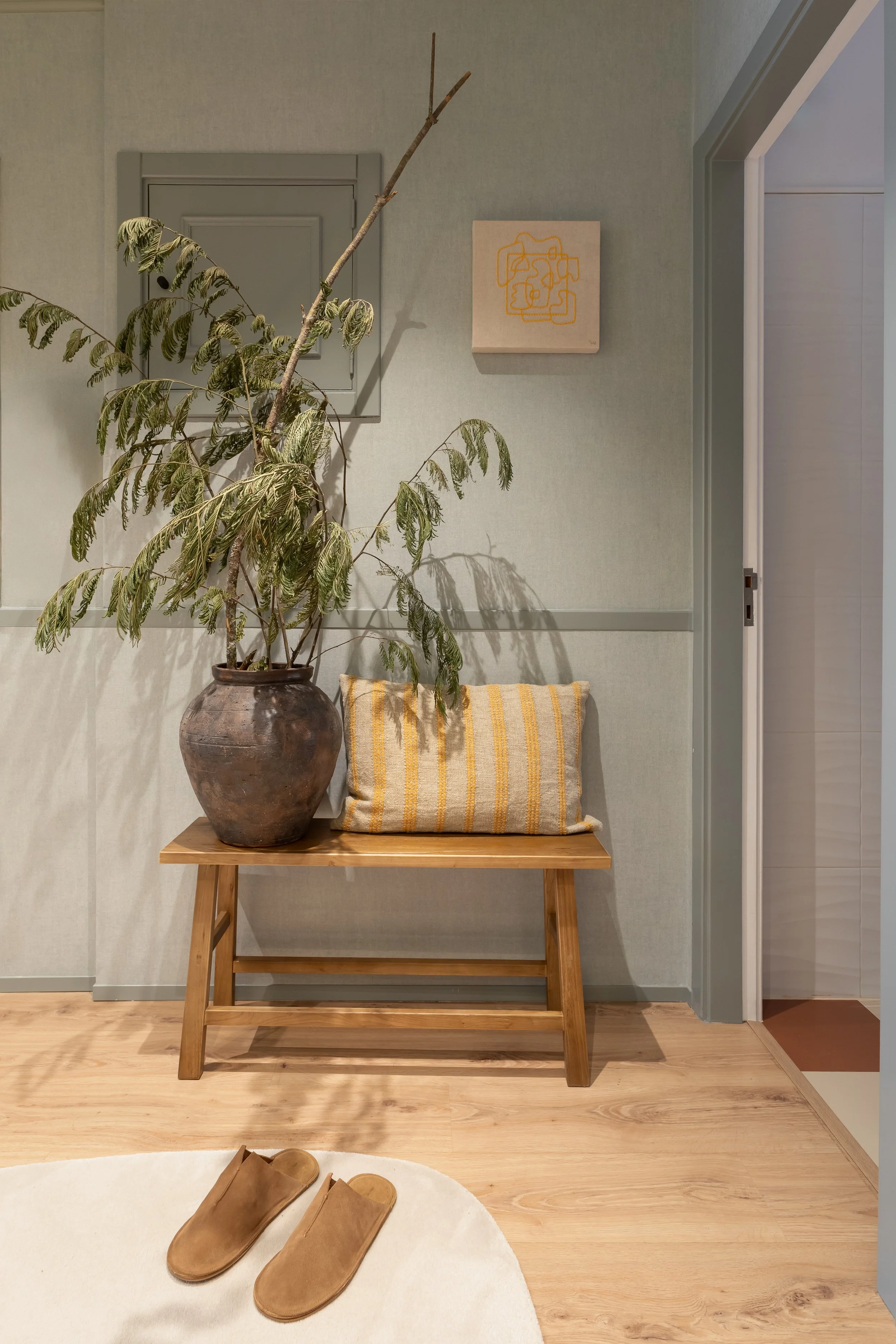 Hall de entrada com banco de madeira, planta de grande porte e quadro