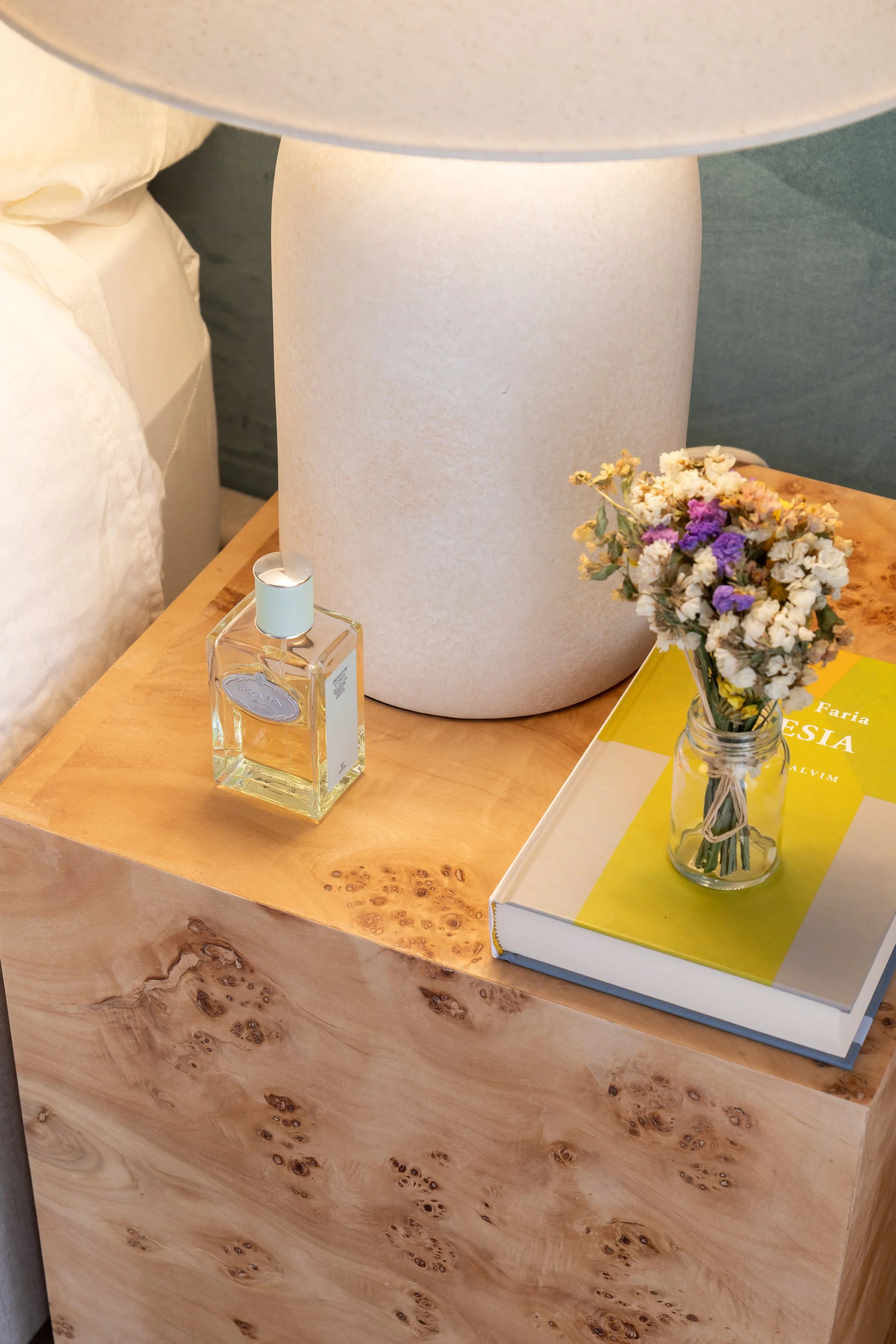 Mesa de apoio em madeira com jarra de flores, livro e candeeiro branco