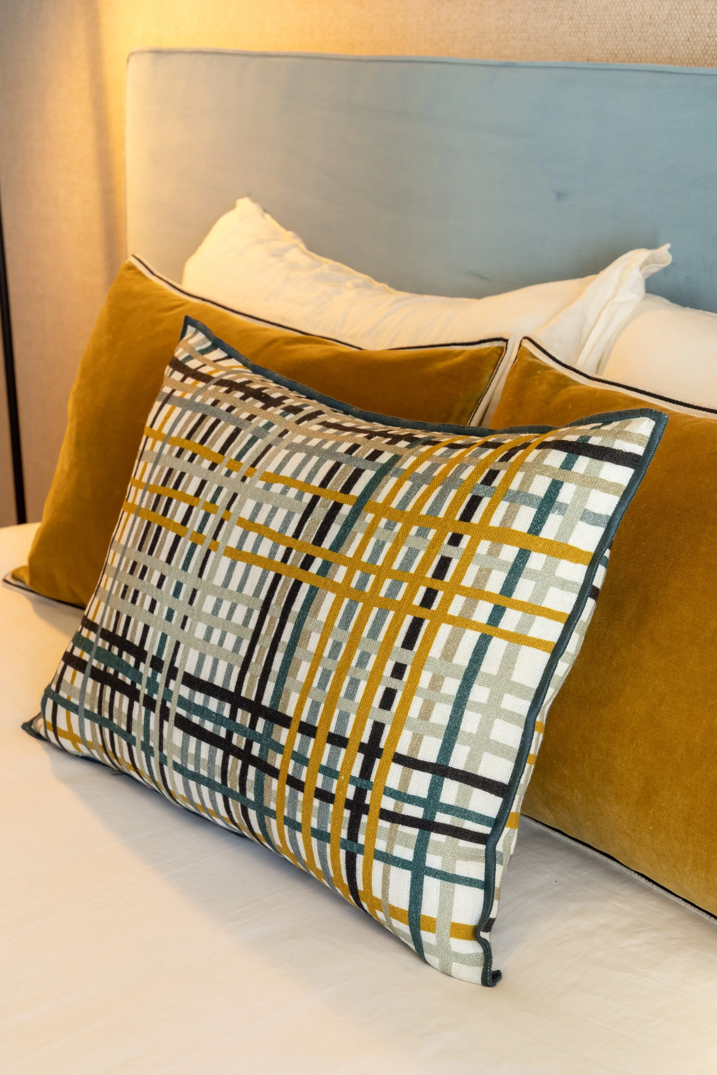 Almofadas decorativas em veludo amarelo e padrão gráfico sobre cama de casal