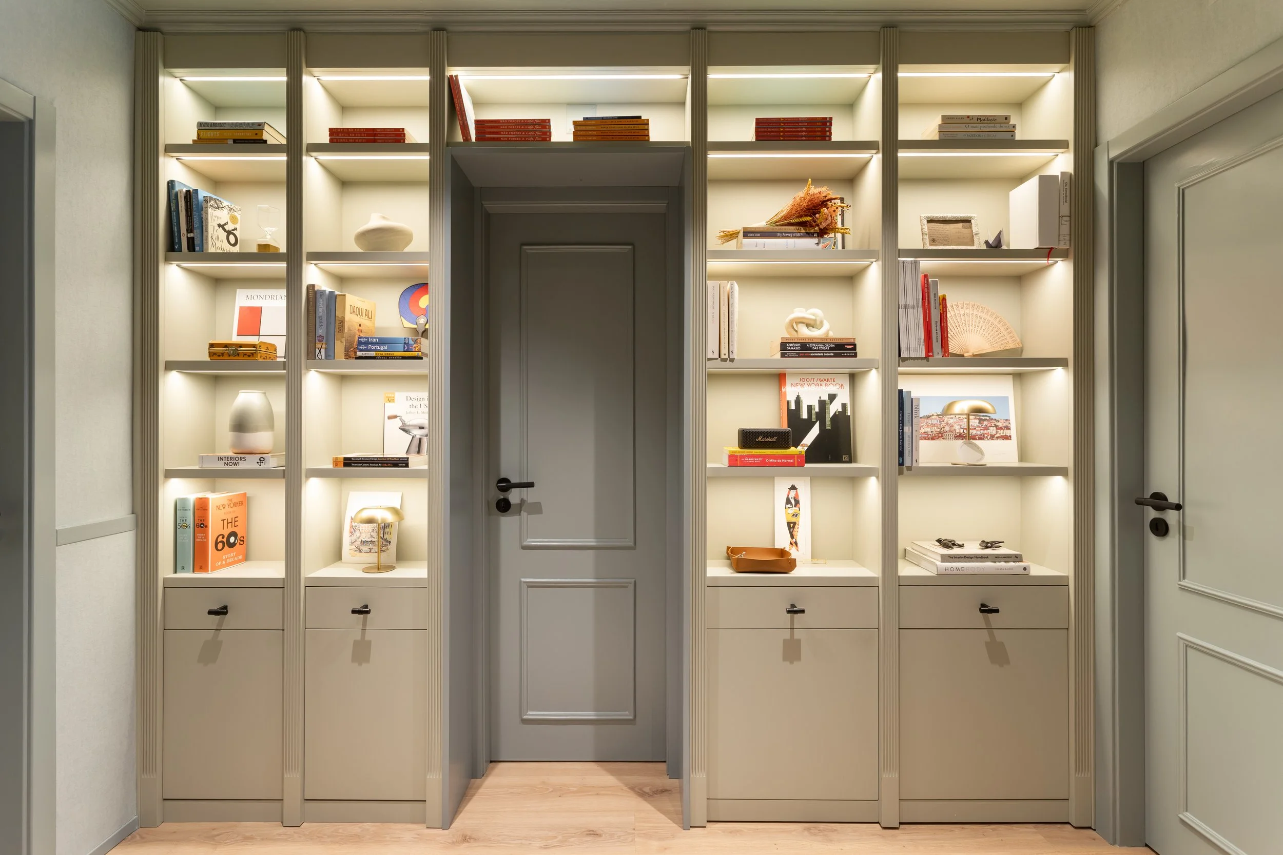 Estante com iluminação embutida, livros e objetos decorativos em hall residencial