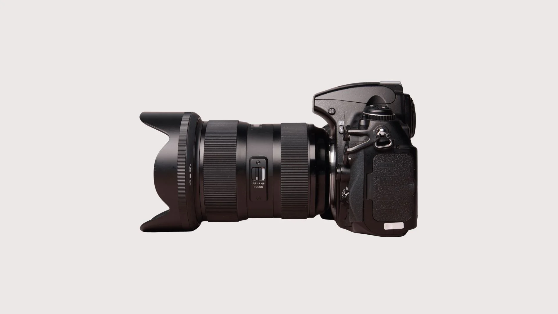 Cámara réflex digital con lente grande y visor, vista lateral en fondo claro.