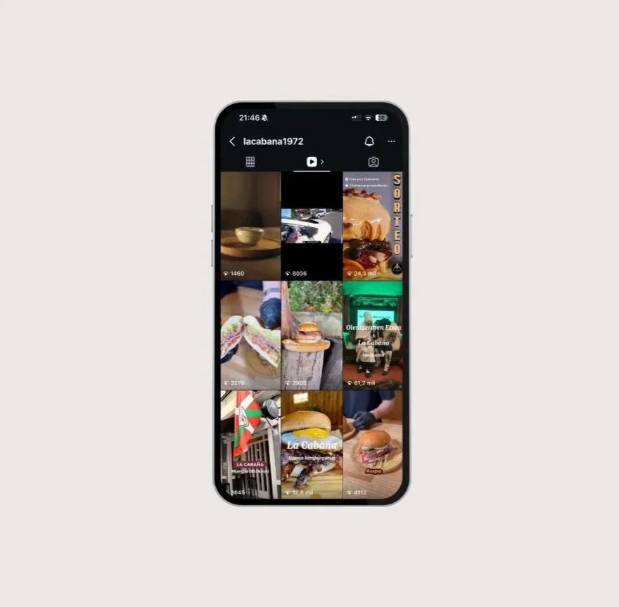Pantalla de teléfono móvil mostrando una cuadrícula de videos relacionados con comida y restaurante, incluyendo hamburguesas, sándwiches, un plato de sopa y otros platillos.