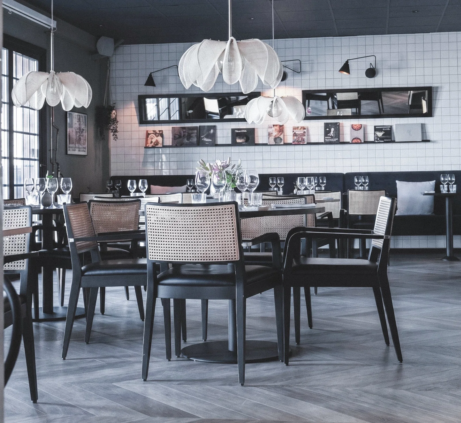 Interiör av en restaurang eller kafé med dukade bord, vinglas, blommor, moderna lampor, speglar och konst på väggarna.