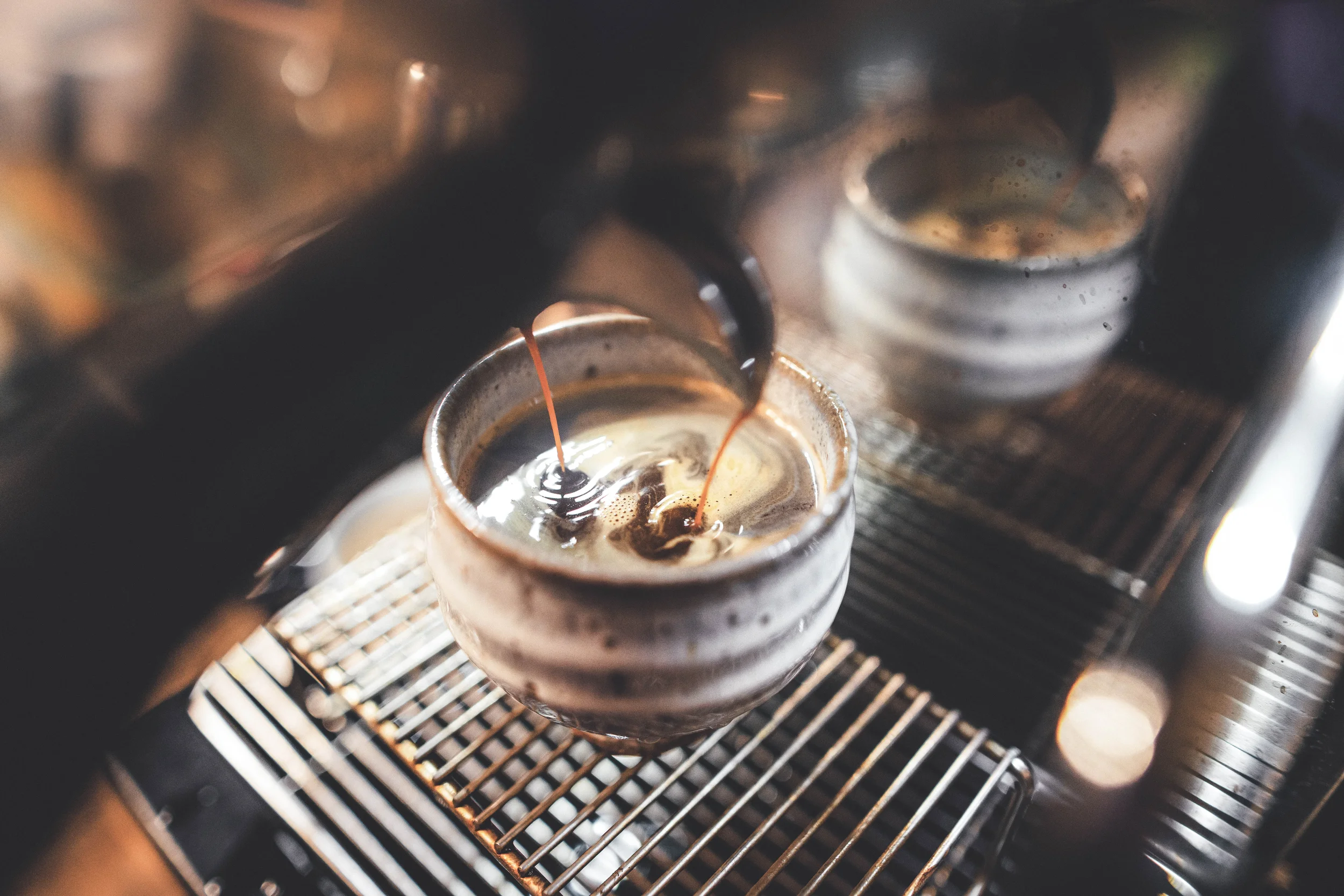 Utsnitt av en kaffemaskin som brygger espresso i koppar på ett galler.