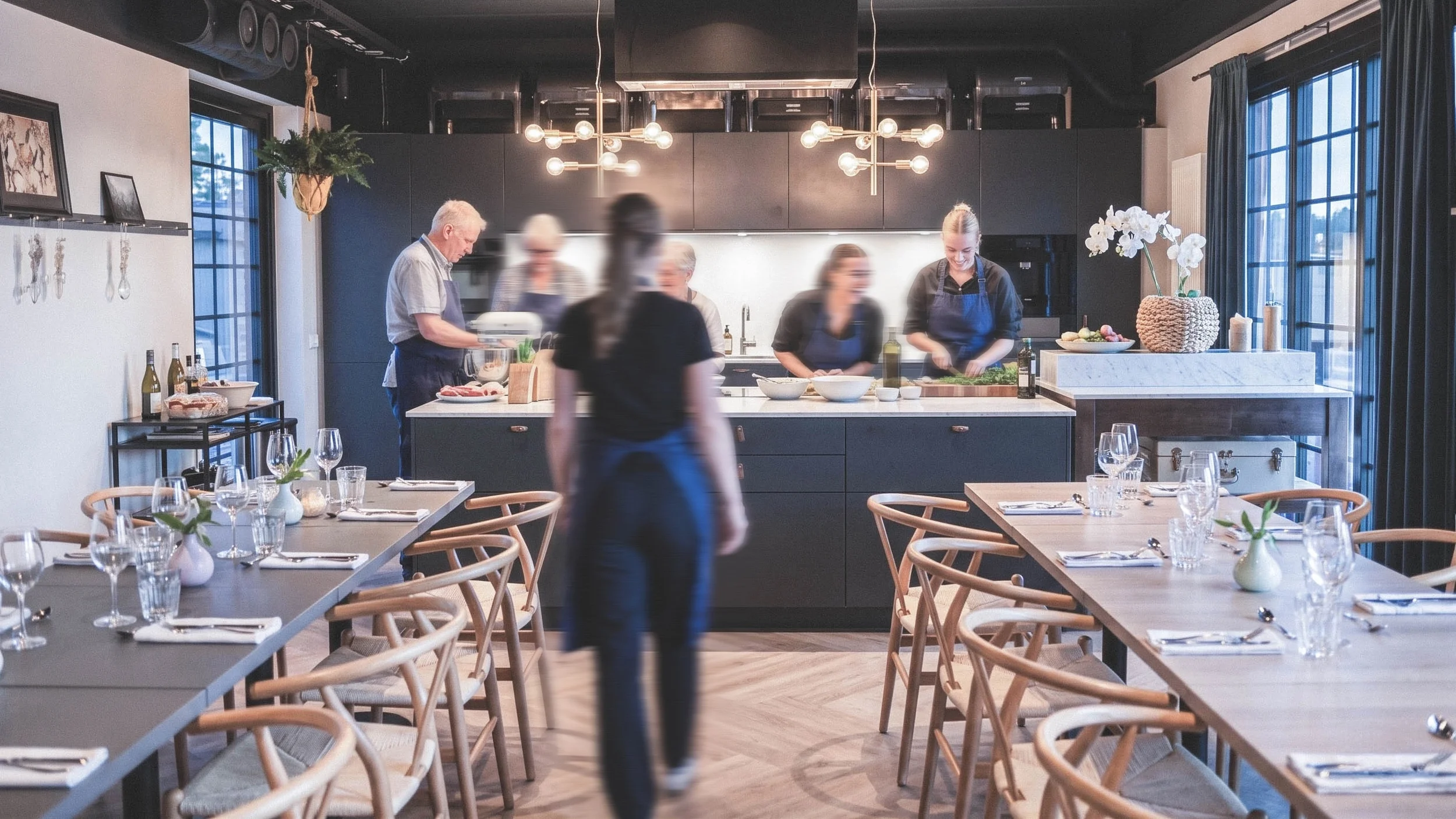 Personer i ett kök och restaurang sammanhang, förberedelse för en måltid, med ett bord dukat för gäster.