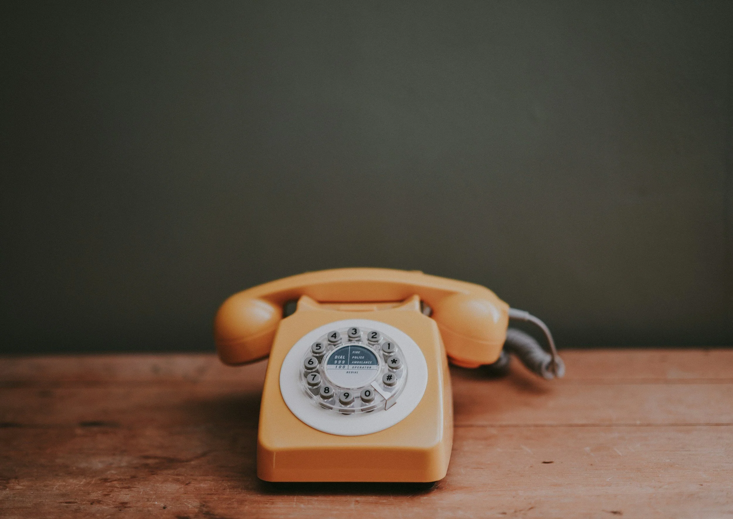 Téléphone orange vintage avec cadran rotatif placé sur une surface en bois. Arrière-plan sombre.