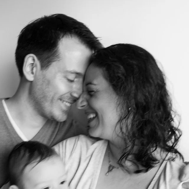 Ein glückliches Paar mit Kleinkind zusammen, lächelnd und sich berührend, in Schwarz-Weiß-Fotografie.