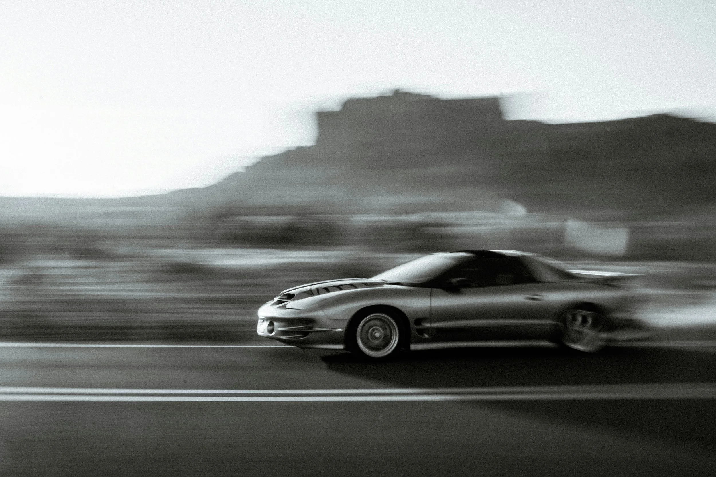 A silver sports car racing on a highway with a blurred background and a large mountain in the distance.