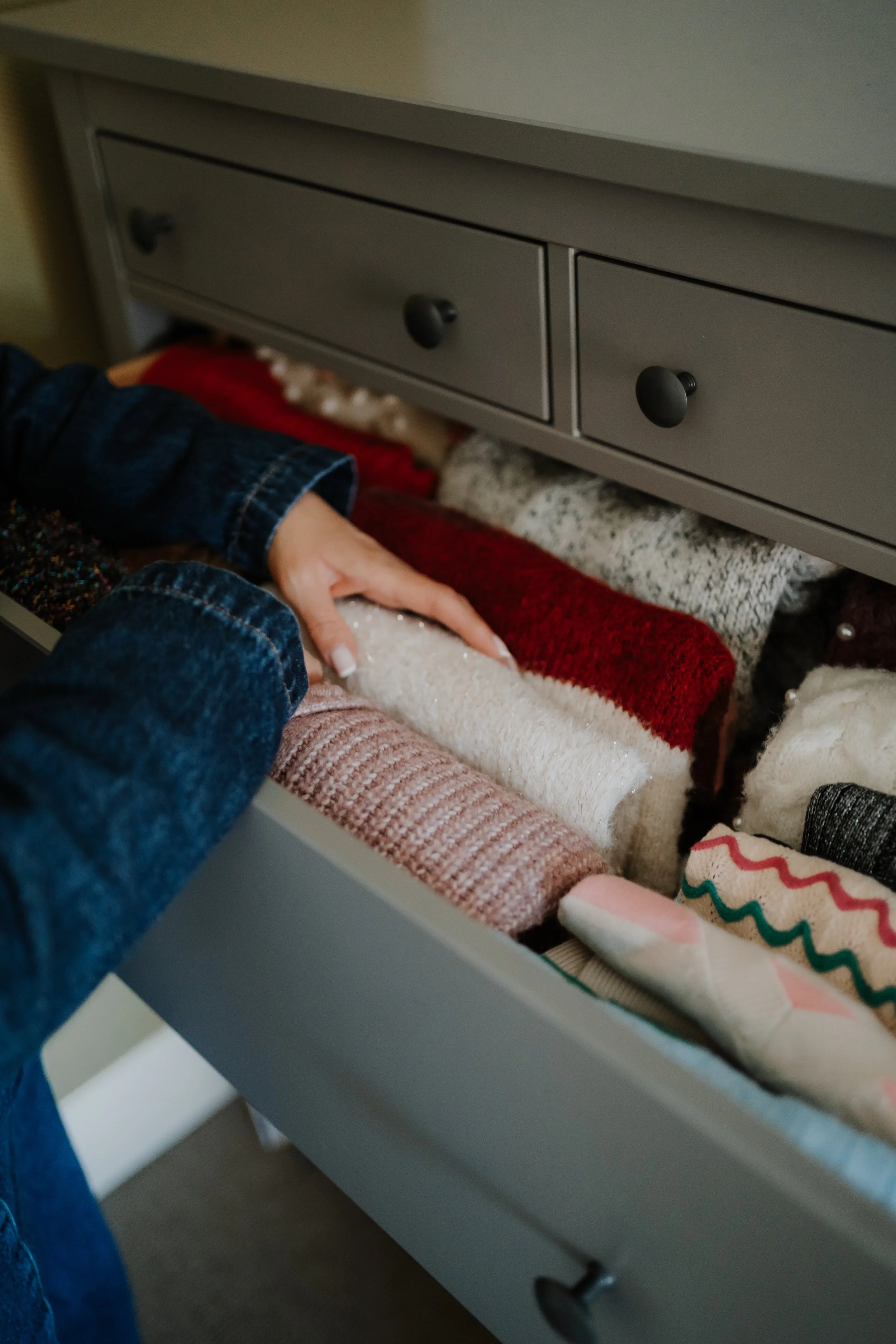 Person organizing colorful sweaters in a drawer.