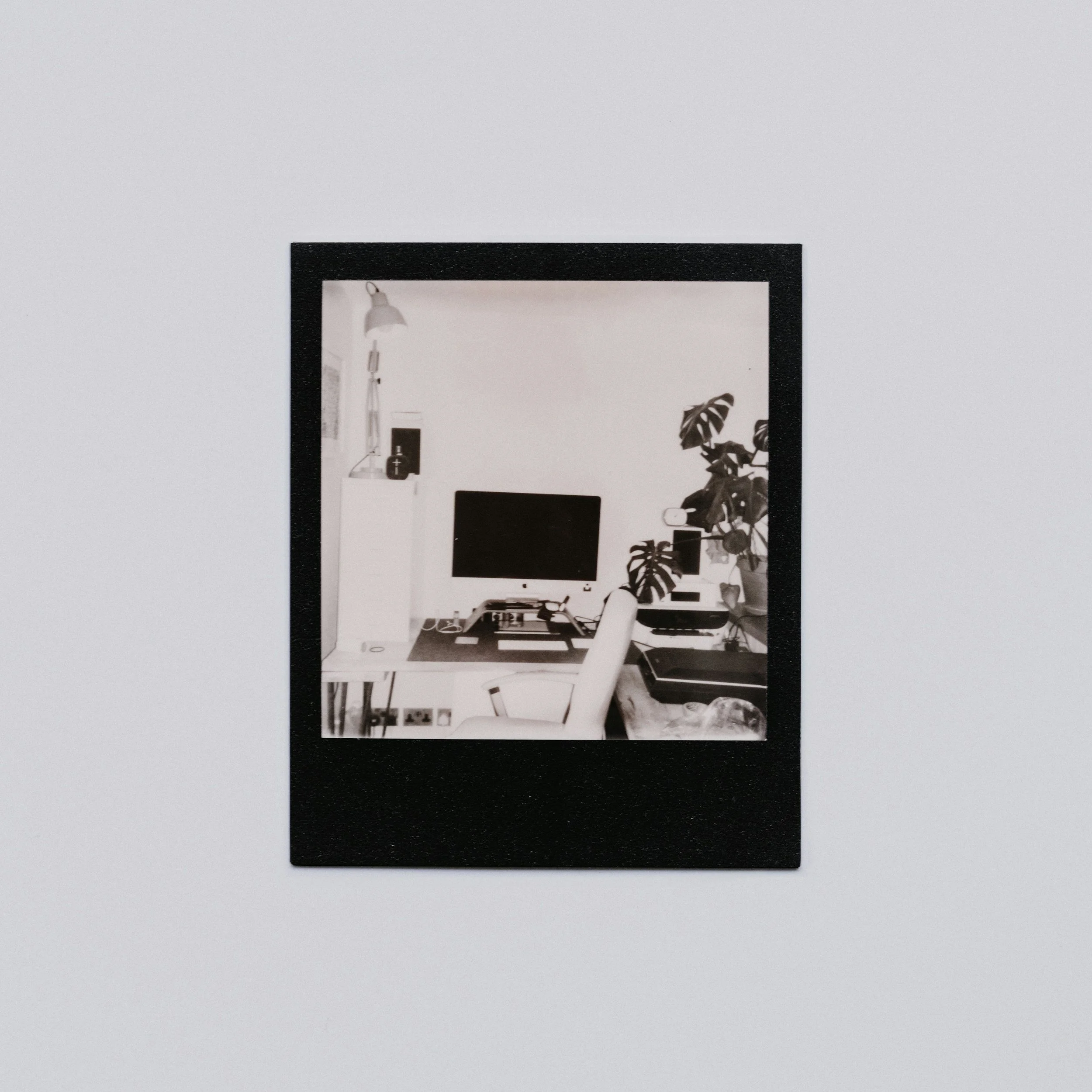 Reflection of a modern office space with a computer monitor and a plant in the mirror.