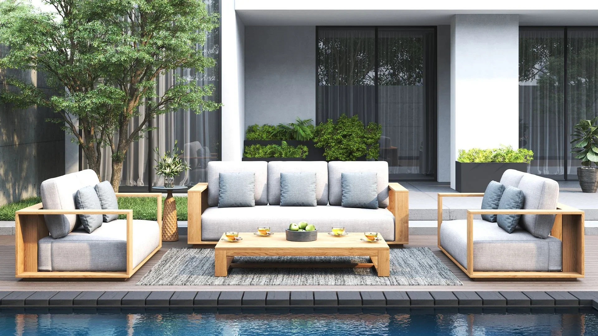 Modern outdoor patio with three light gray cushioned sofas with wooden frames, a wooden coffee table with tea cups and apples, a tall gourd-shaped vase, and background of glass sliding doors, plants, and a tree.