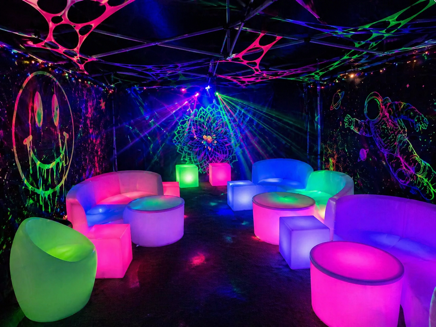 A neon-lit lounge with glowing furniture in pink, green, and blue, surrounded by black walls decorated with glowing space-themed and geometric designs including a smiley face and an astronaut.