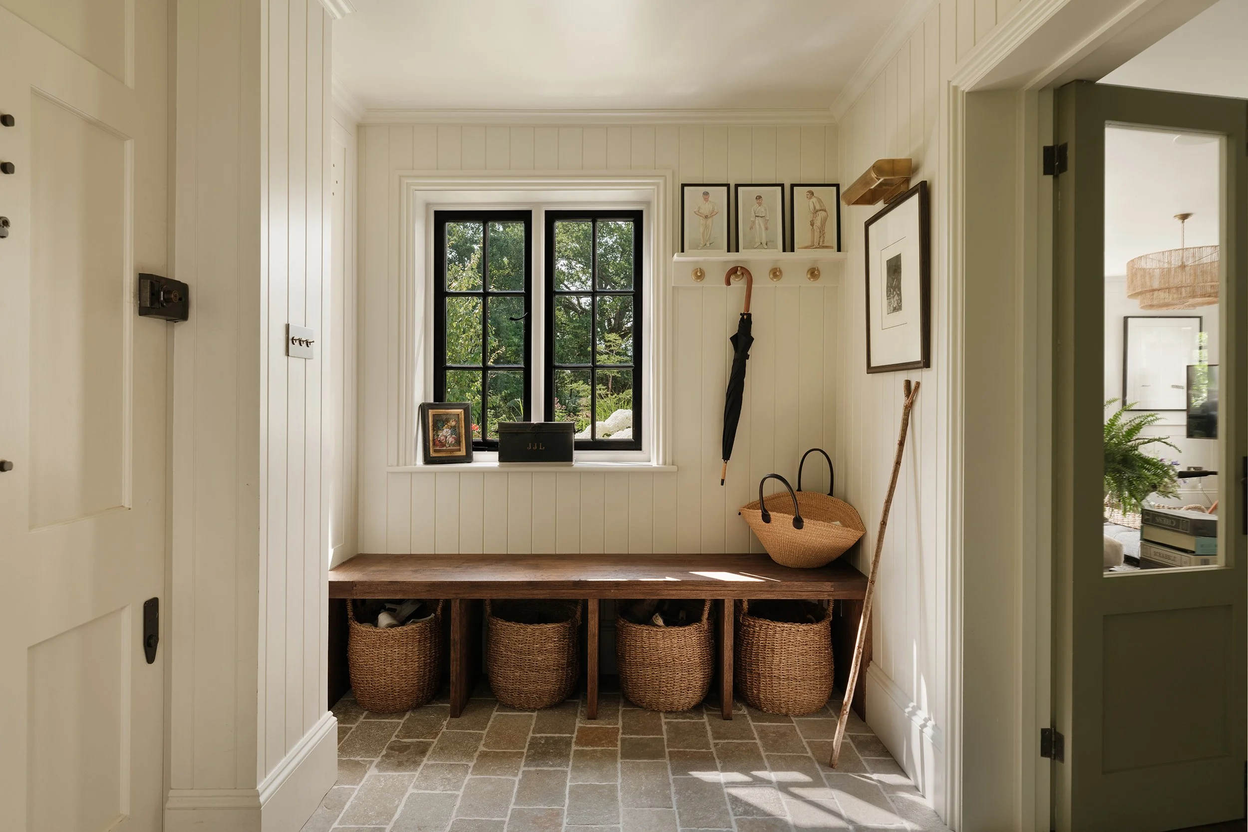 Entryway with a window, baskets beneath a wooden countertop, framed pictures on the wall, and cleaning tools like an umbrella, broom, and mop.