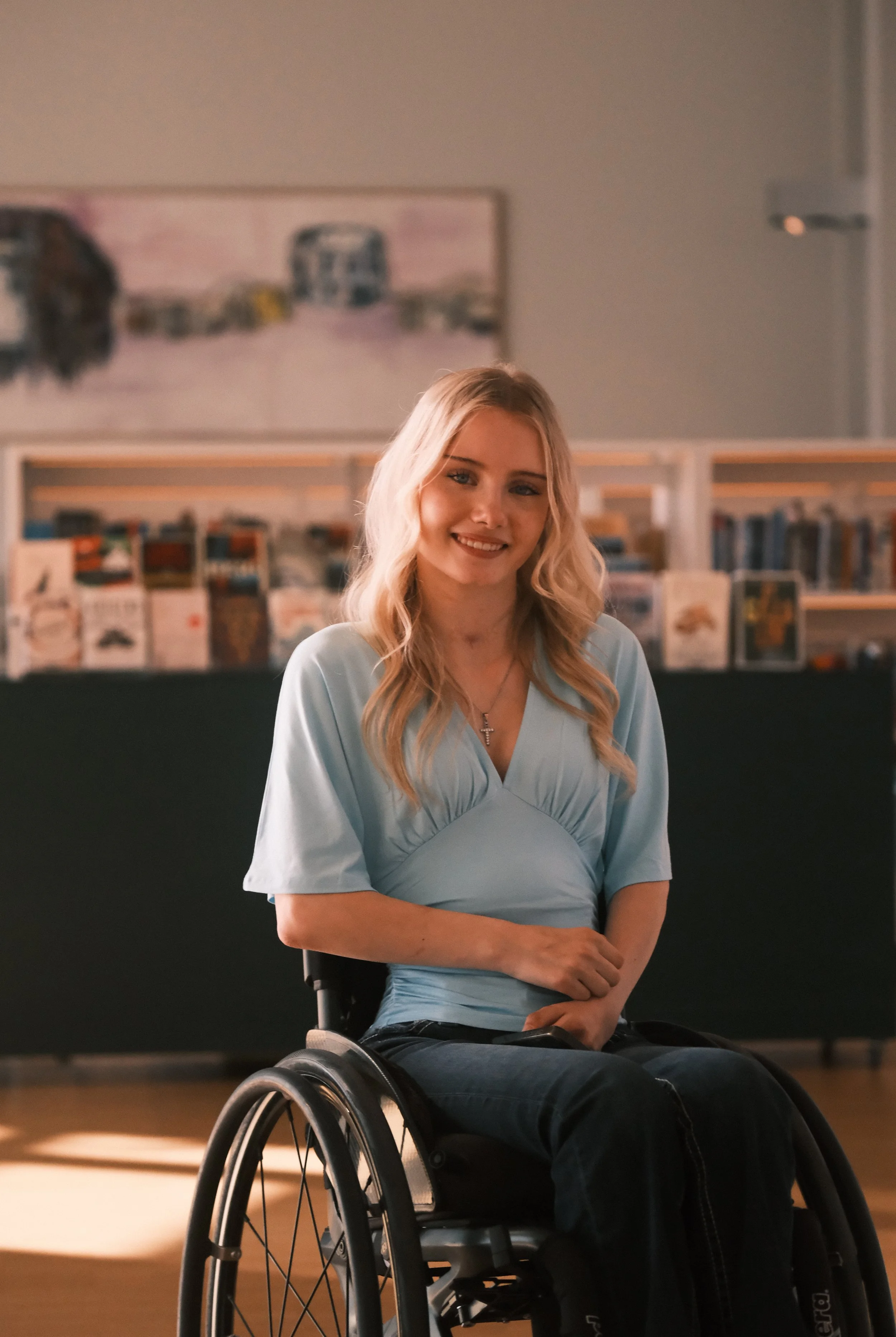Elise sitter i rullestol og smiler mot kamera.