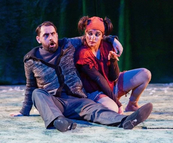 Conall O'Neill, Bass, Cunning Little Vixen. Two performers on stage during a theatrical performance, one man and one woman sitting on a stage with a forest backdrop, expressing intense emotions.
