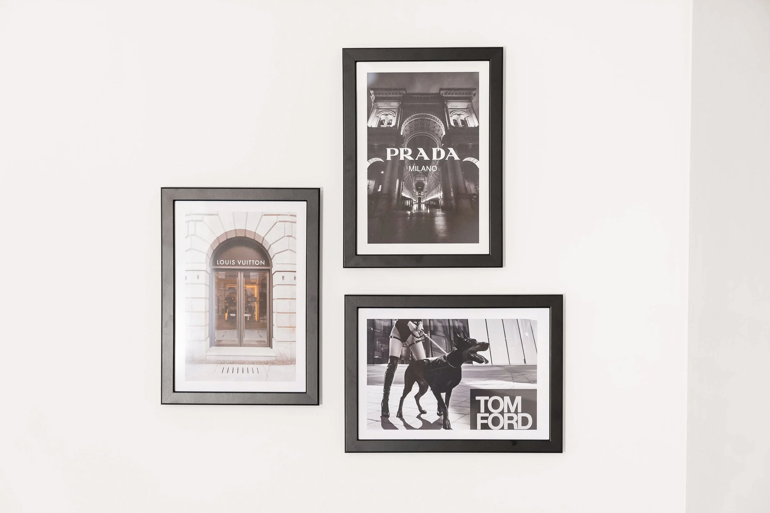 Gallery wall with four framed photographs, including images of luxury brands and a dog with a woman, in a room with white wall.