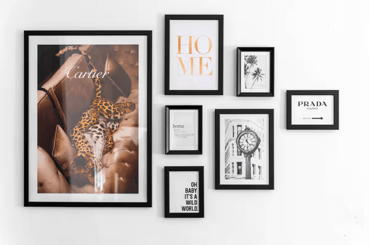 Gallery wall with eight black-framed pictures, including a leopard poster, the word "HOME," a palm tree illustration, a clock photo, and inspirational quotes.