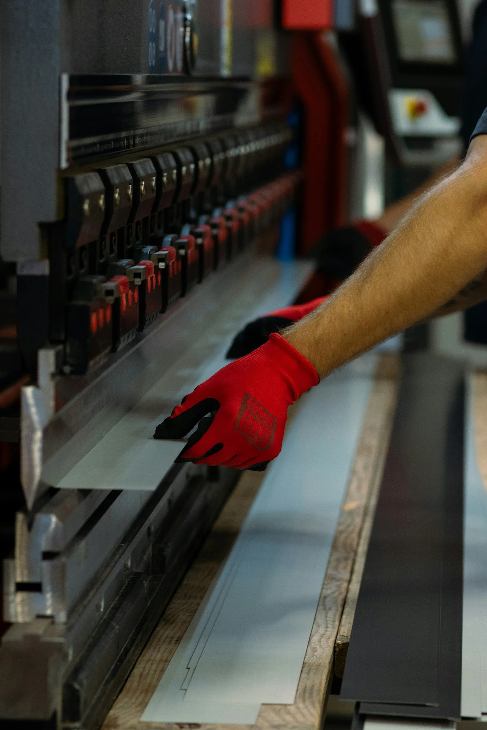 Person wearing red gloves working with a machine that appears to be processing or printing white sheets of paper or material.