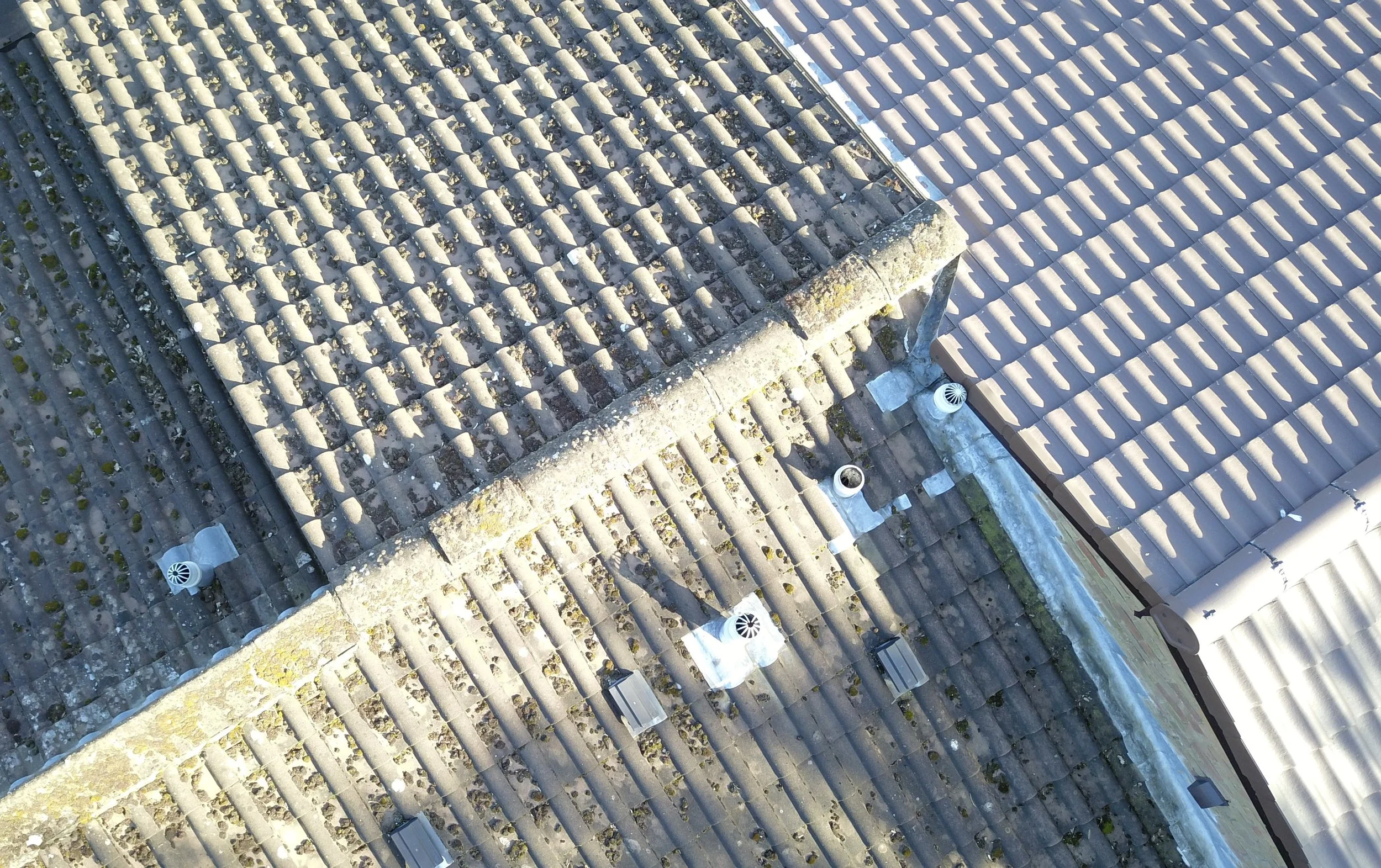 A roof with two sections of tiles, one older and covered with moss, the other newer and clean, with visible vents.