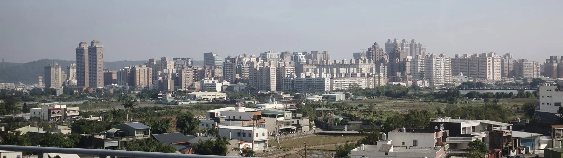 Taoyuan City skyline with high-rise buildings in the background and smaller houses in the foreground, with some greenery and a body of water to the side