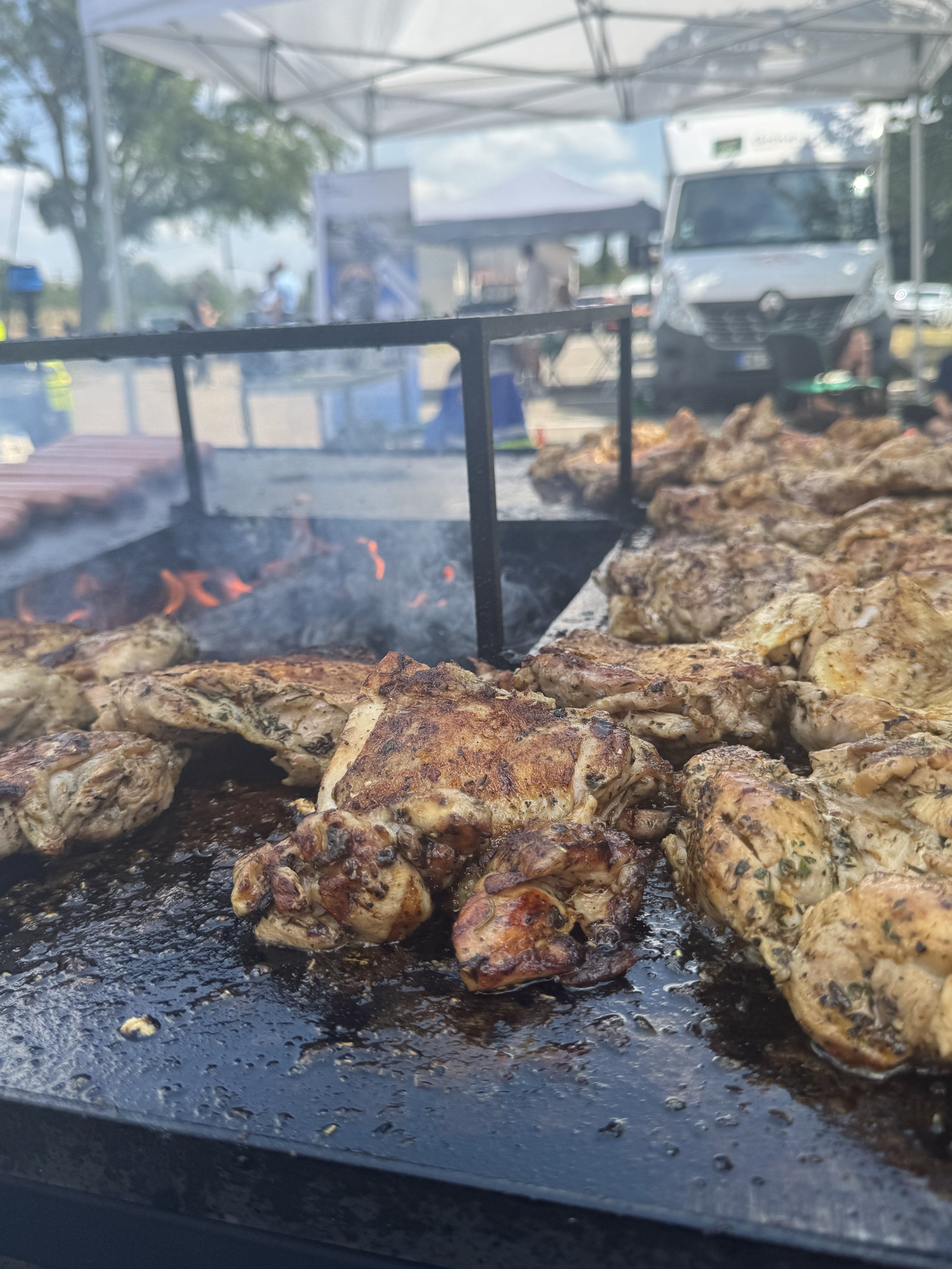 Viande grillée en train de cuire sur un barbecue, avec un fond flou d'un marché en plein air.