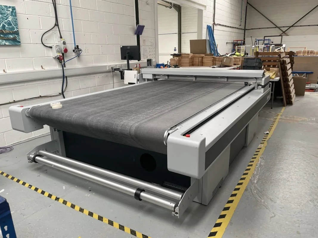 Zünd G3 Cutter Werxco cutting machine at a printers, surrounded by stacks of cardboard and plywood.