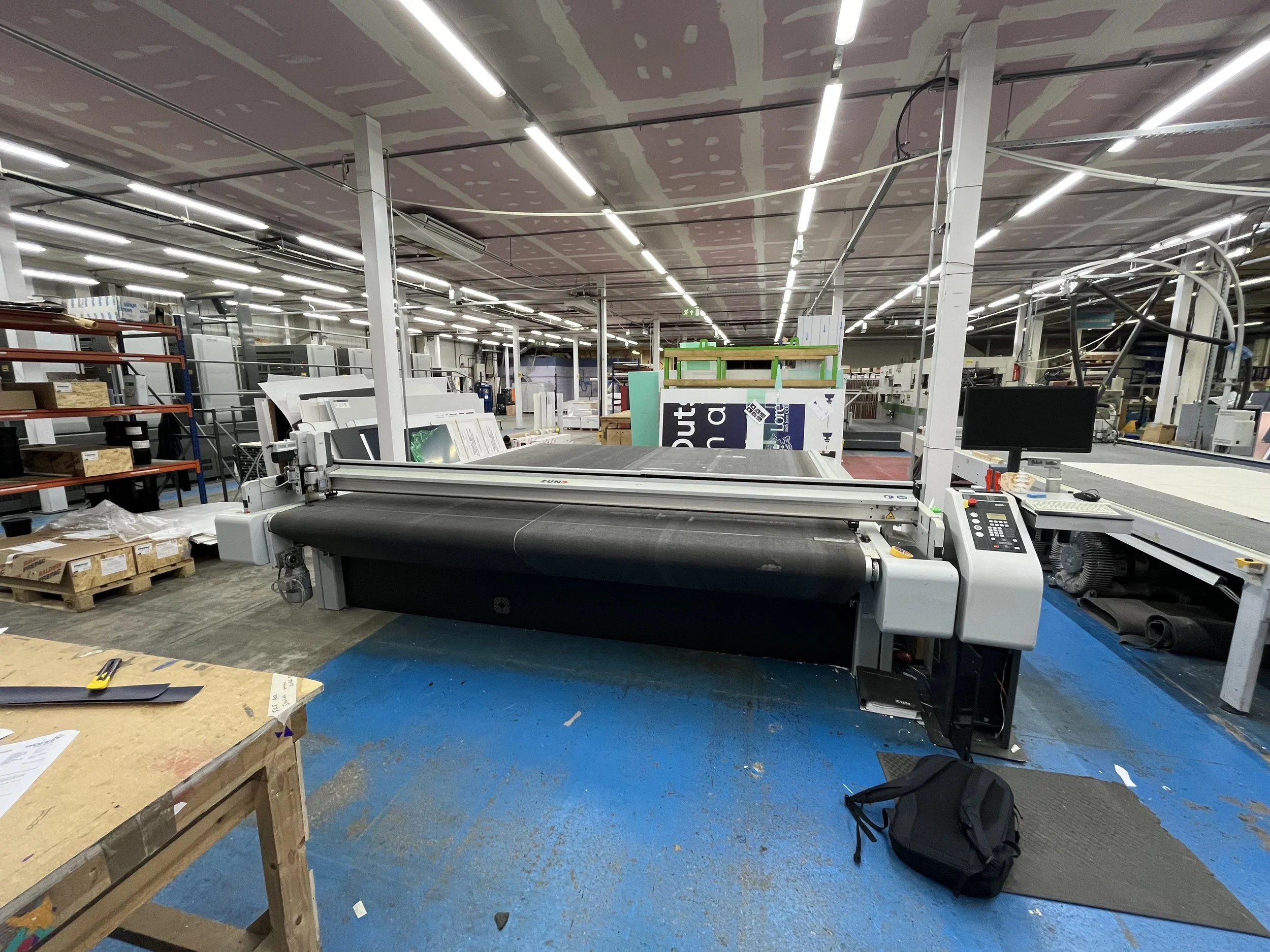 Zund S3 Large Format Cutting Table in a printers workspace with various machinery and materials.