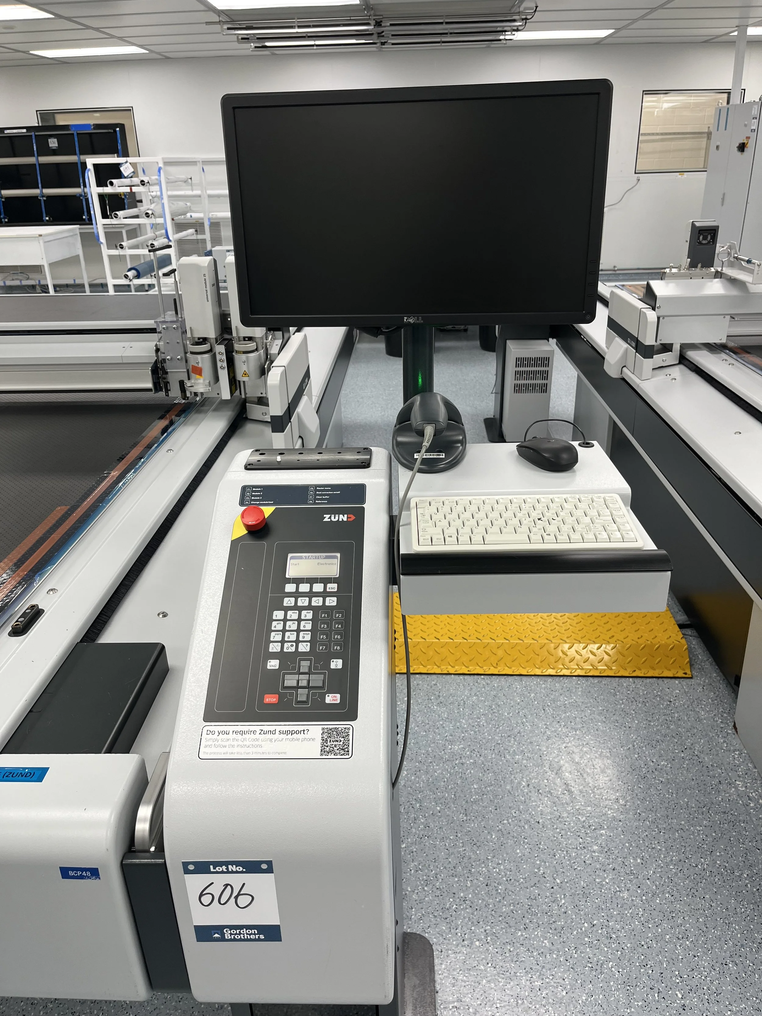 A piece of industrial equipment in a clean, well-lit room. It has a control panel with a red emergency stop button, a keypad, a monitor, and various connected devices. The equipment is marked with the lot number 606 and the brand Gordon Brothers.