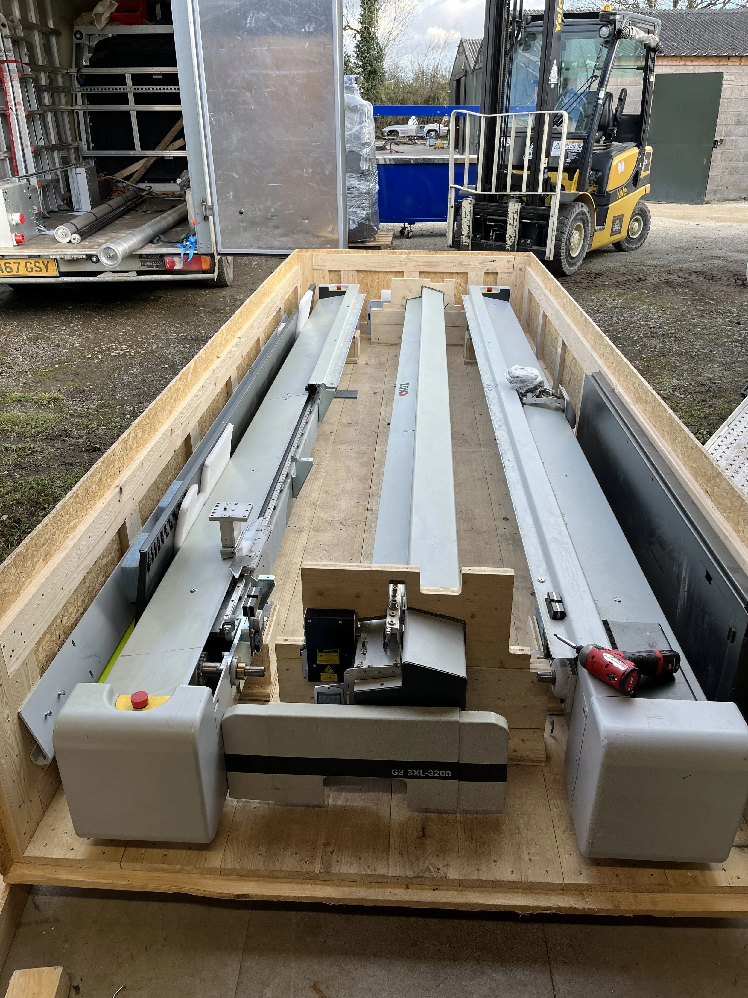 A woodworking or manufacturing setup in a wooden framed workstation, with metal and electronic equipment, including a power drill, on a table within a workshop or industrial setting.