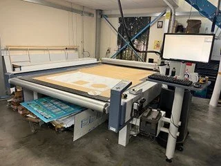 Large industrial flatbed cutter with a computer station in a workshop setting.